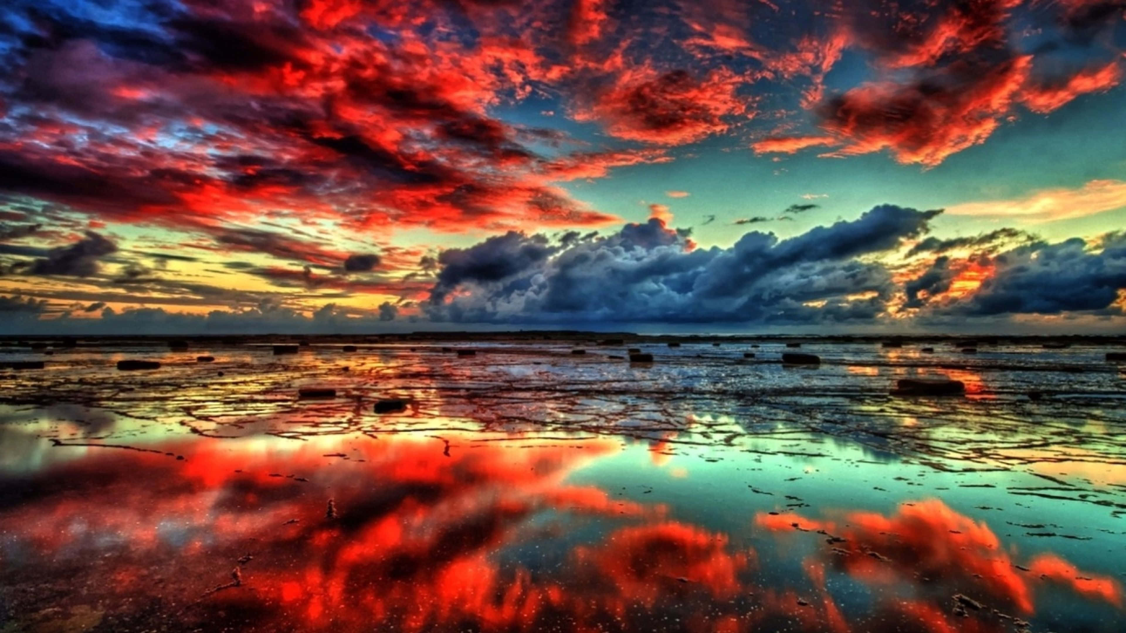 reflection 桌布 壁紙 — 鮮豔的紅色和藍色雲彩在平坦地平線上的戲劇性日落中倒映在淺水中。