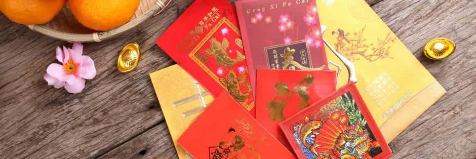 Red Envelope 桌布 壁紙 — 鮮豔的紅色和金色中國新年紅包帶有節日設計，放在質樸的木桌上，旁邊有橙子和粉紅色的櫻花。