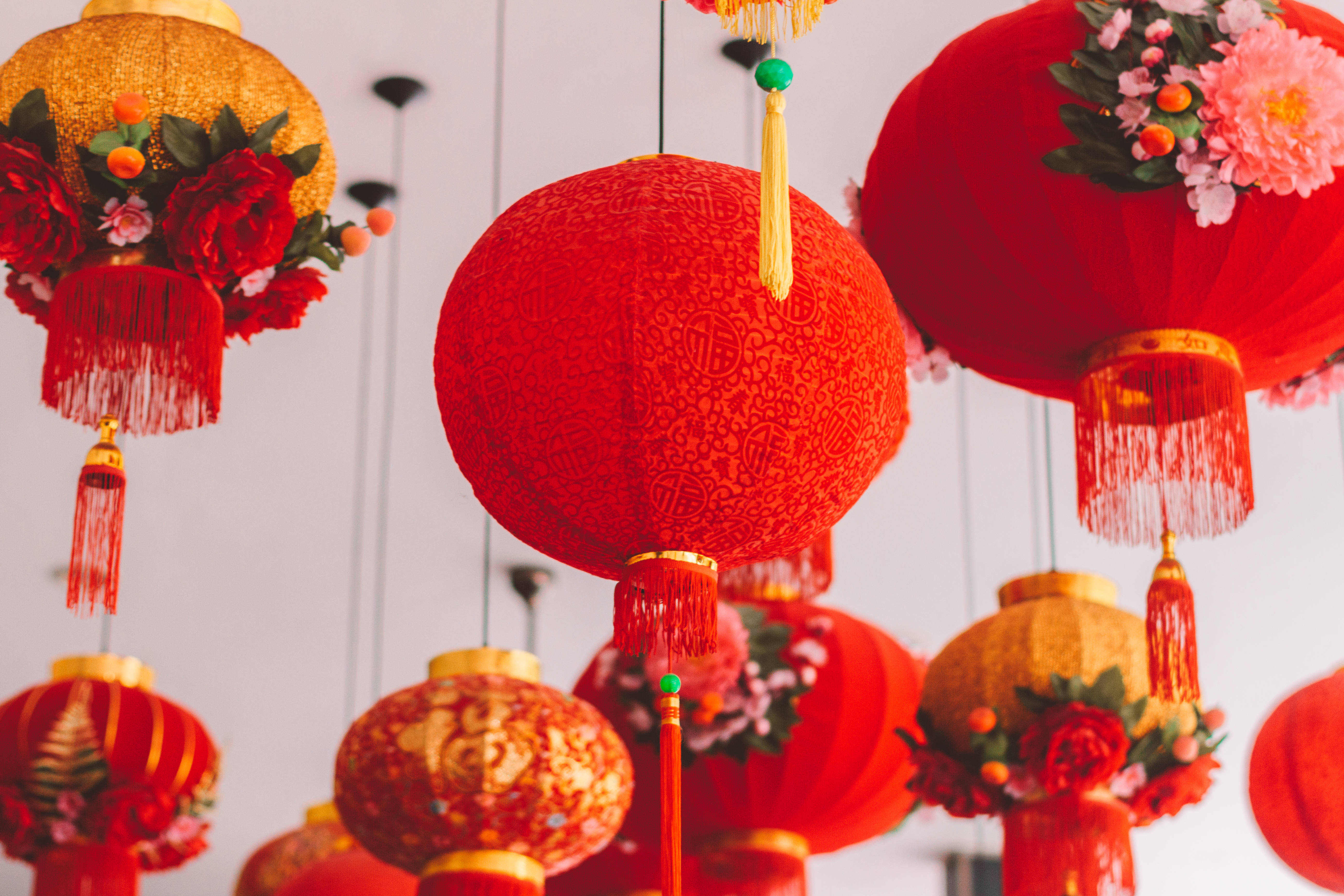 春節 桌布 壁紙 — 鮮豔的紅色和金色中國燈籠，飾有花朵和流蘇，懸掛在明亮的白色背景上，形成節日簇。