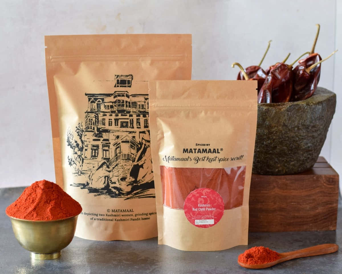Red Chili Powder 桌布 壁紙 — 鮮豔的紅色喀什米爾辣椒粉放在黃銅碗中，旁邊有品牌香料袋和石臼中的乾辣椒。