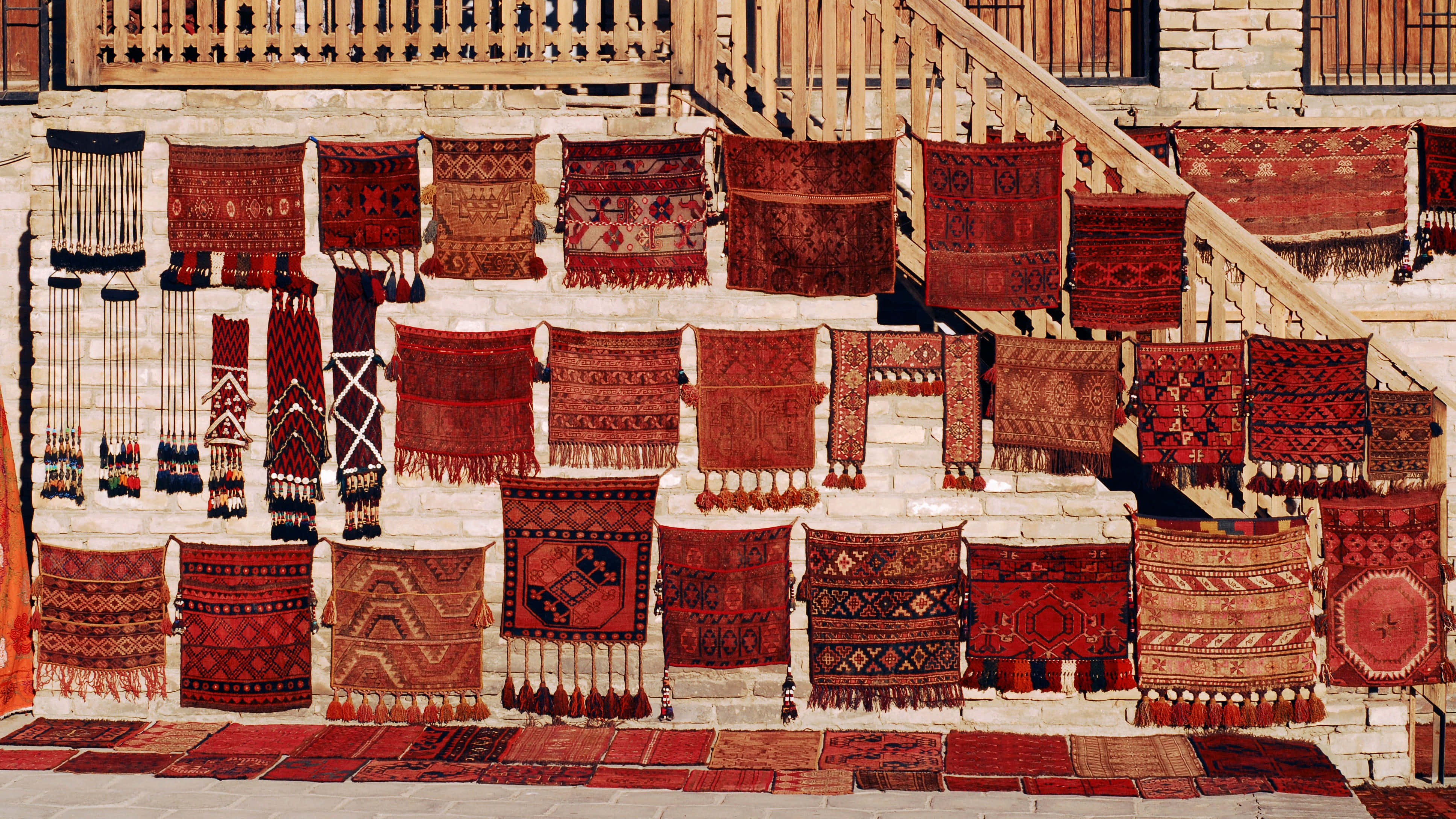Carpet 桌布 壁紙 — 鮮豔的紅色圖案地毯密集地掛在風化的石牆上，旁邊是木樓梯。