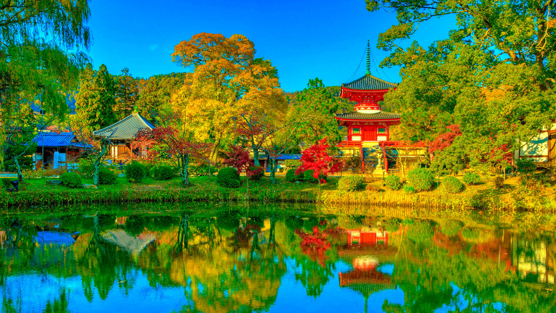 日式自然壁紙 桌布 壁紙 — 鮮豔的紅色寶塔和傳統建築倒映在寧靜的池塘中，周圍是秋天的樹木，天空清澈湛藍。