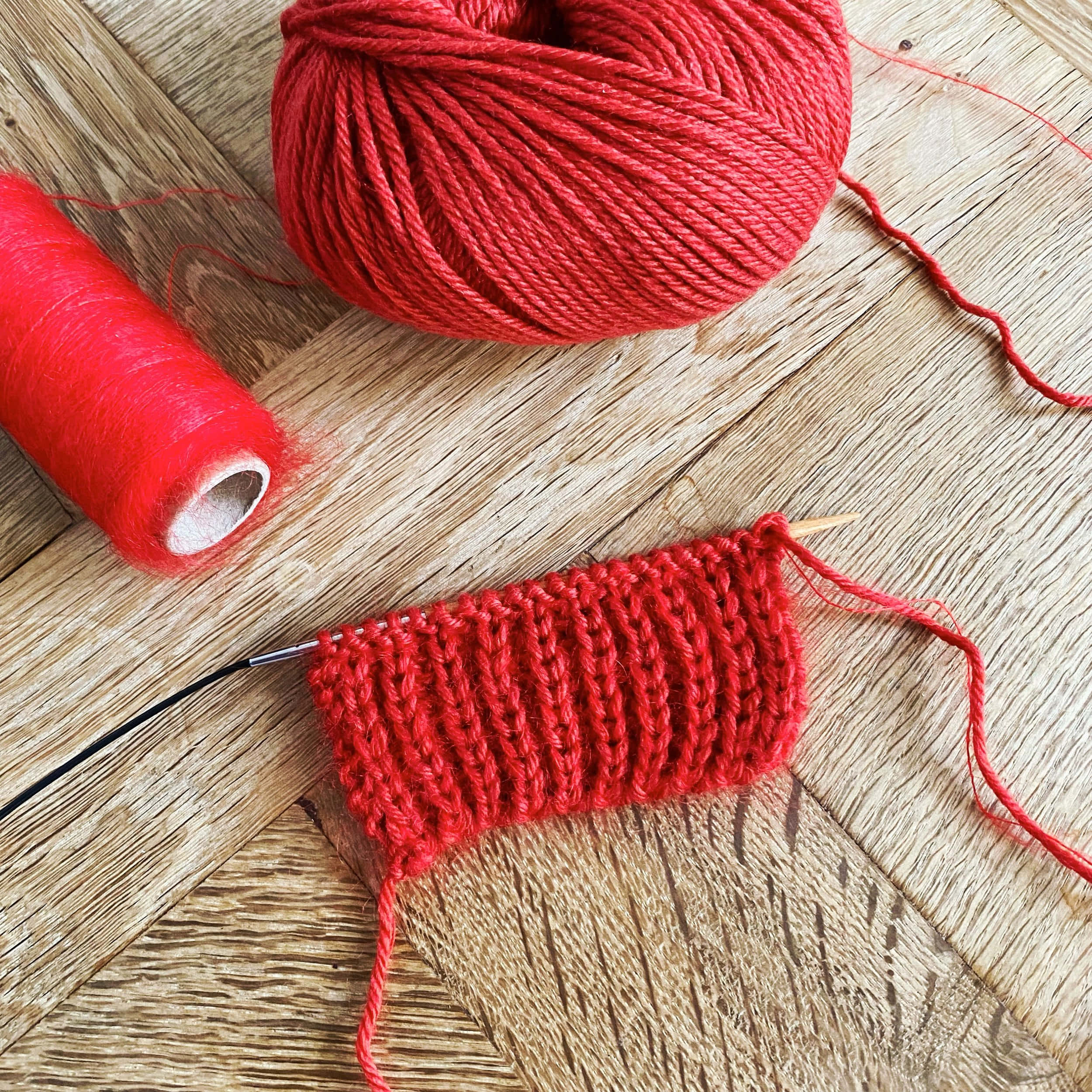 Knitting 桌布 壁紙 — 鮮豔的紅色毛線和編織樣本放在質樸的木質表面上，展示手工紡織工藝。