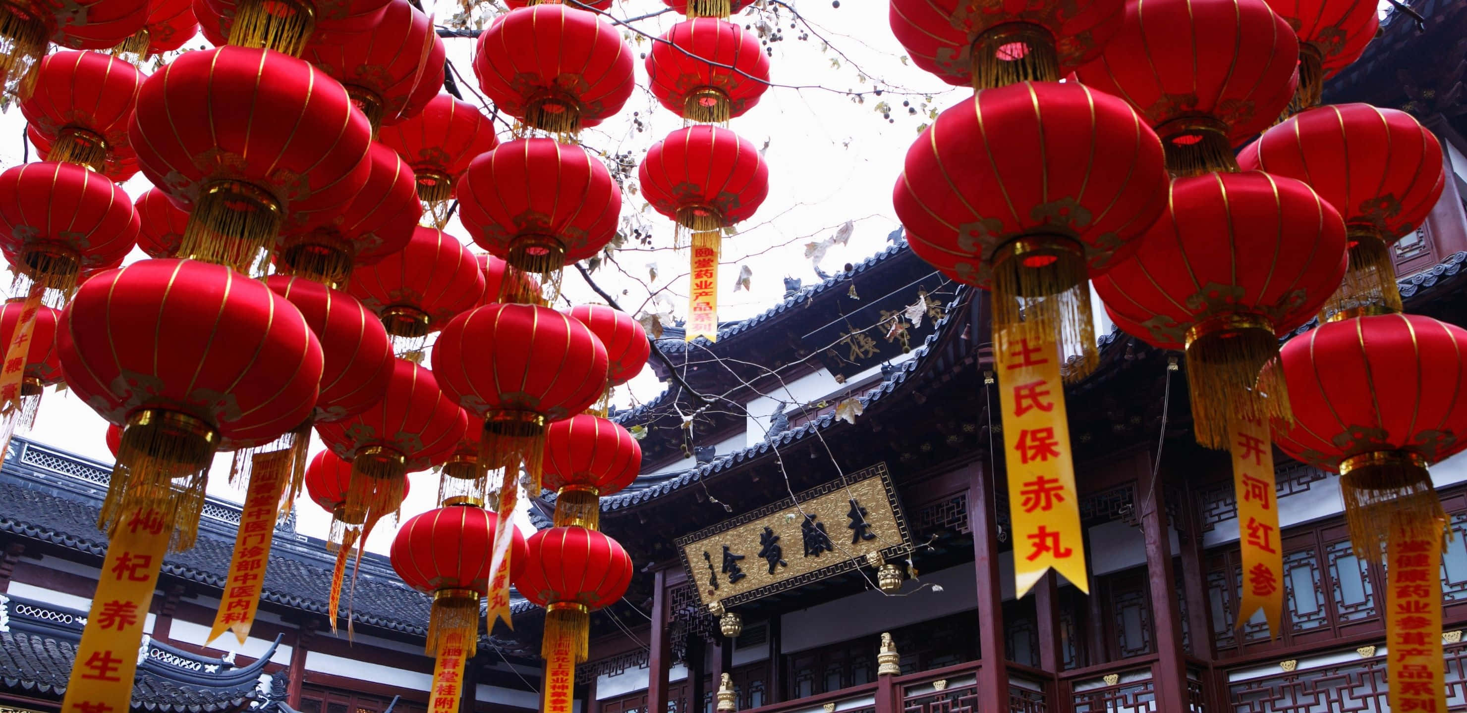 2960x1440 桌布 壁紙 — 鮮豔的紅色燈籠密集地掛在傳統中式寺廟前，寺廟擁有華麗的木結構建築和金色橫幅。