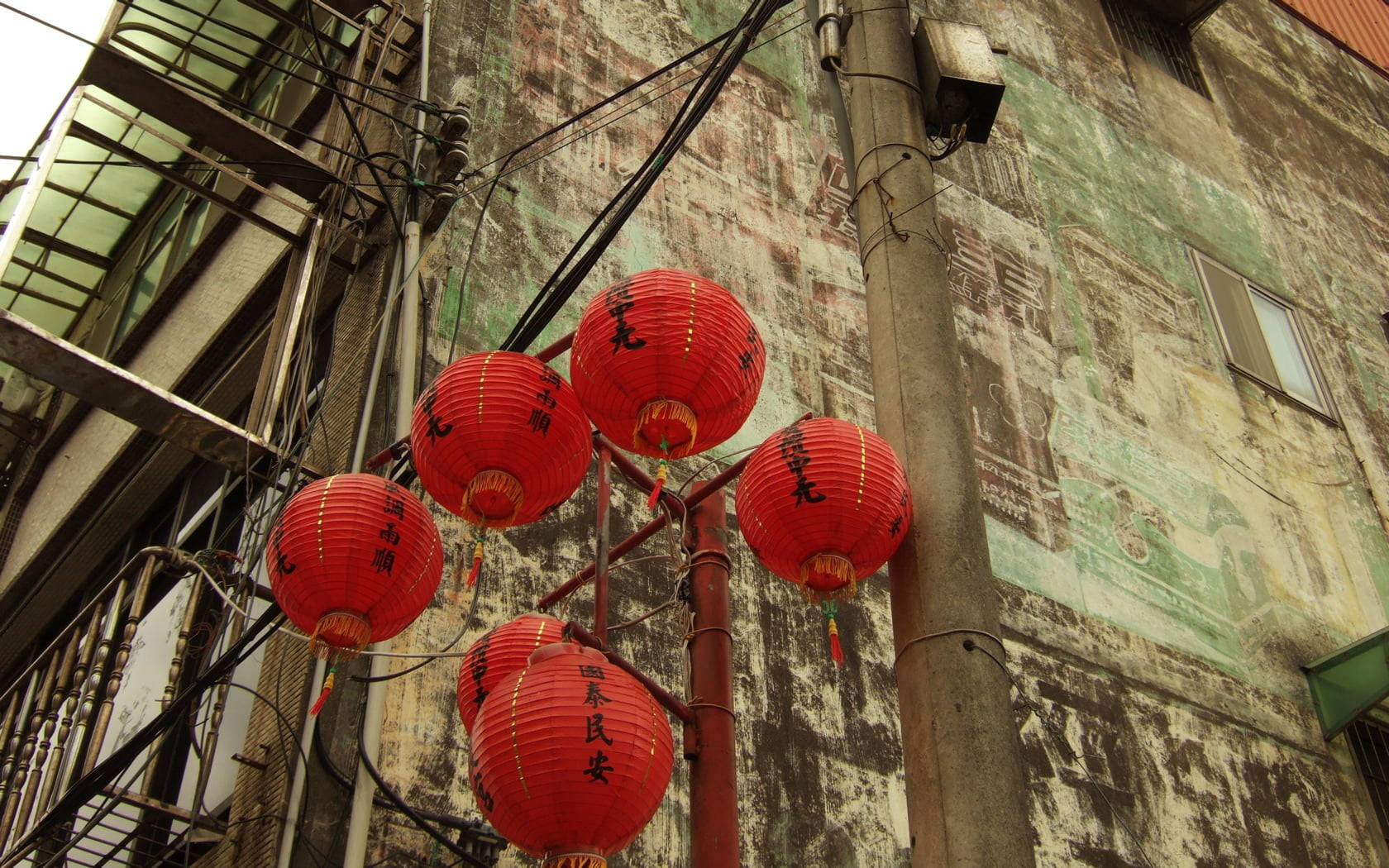 中式房屋壁紙 桌布 壁紙 — 鮮豔的紅色燈籠掛在一個風化的城市小巷牆上，牆上覆蓋著褪色的綠色海報和纏繞的電線。