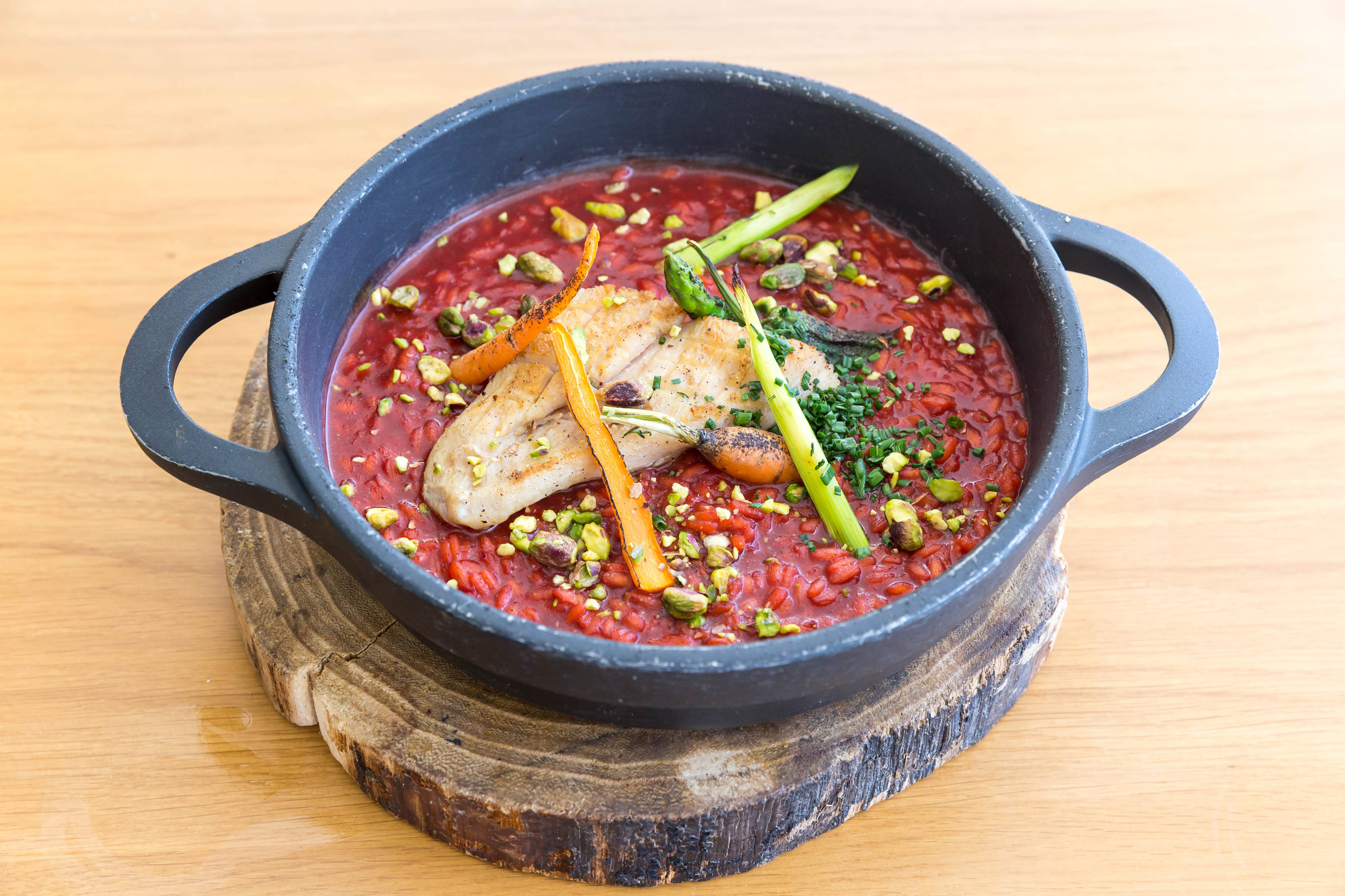 beetroot 桌布 壁紙 — 鮮豔的紅色燉飯搭配烤雞、開心果和蘆筍，盛載於黑色陶瓷鍋中，置於質樸木板上。