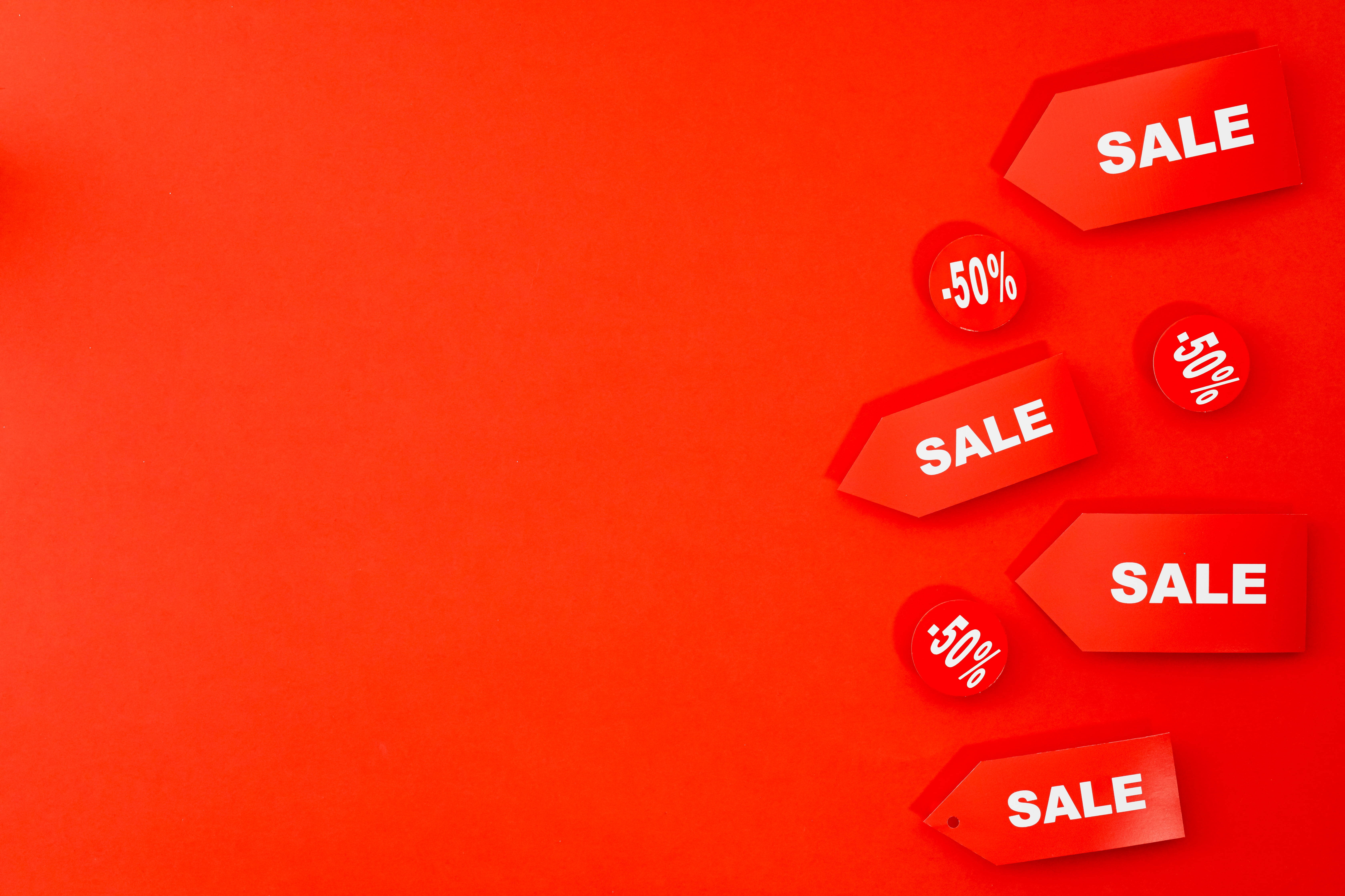 Sales 桌布 壁紙 — 鮮豔的紅色背景，帶有光澤的銷售標籤和折扣貼紙聚集在角落。