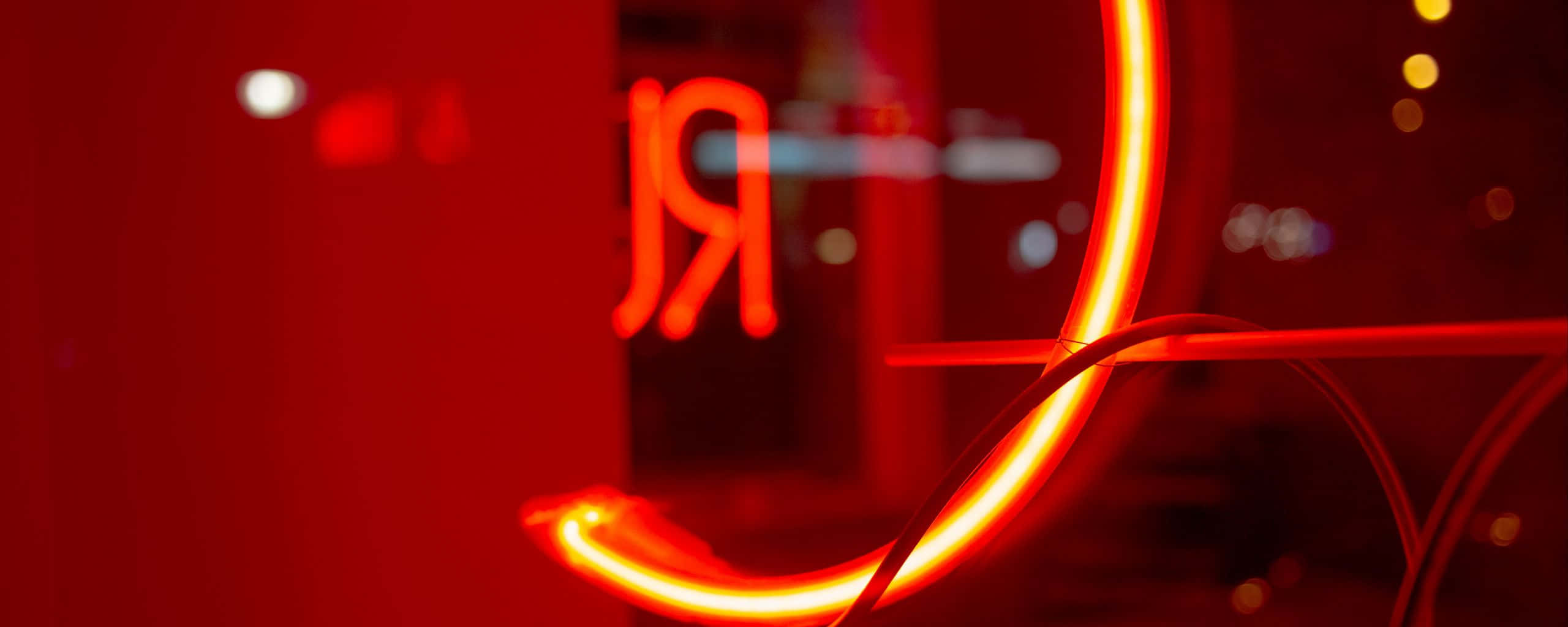 Neon Red Aesthetic 桌布 壁紙 — 鮮豔的紅色霓虹燈招牌在黑暗模糊的城市背景中彎曲發光，帶有散景燈光。