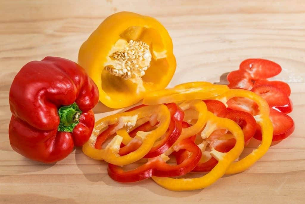 Fruit 桌布 壁紙 — 鮮豔的紅黃甜椒，完整和切片，藝術地擺放在淺色木質表面上。