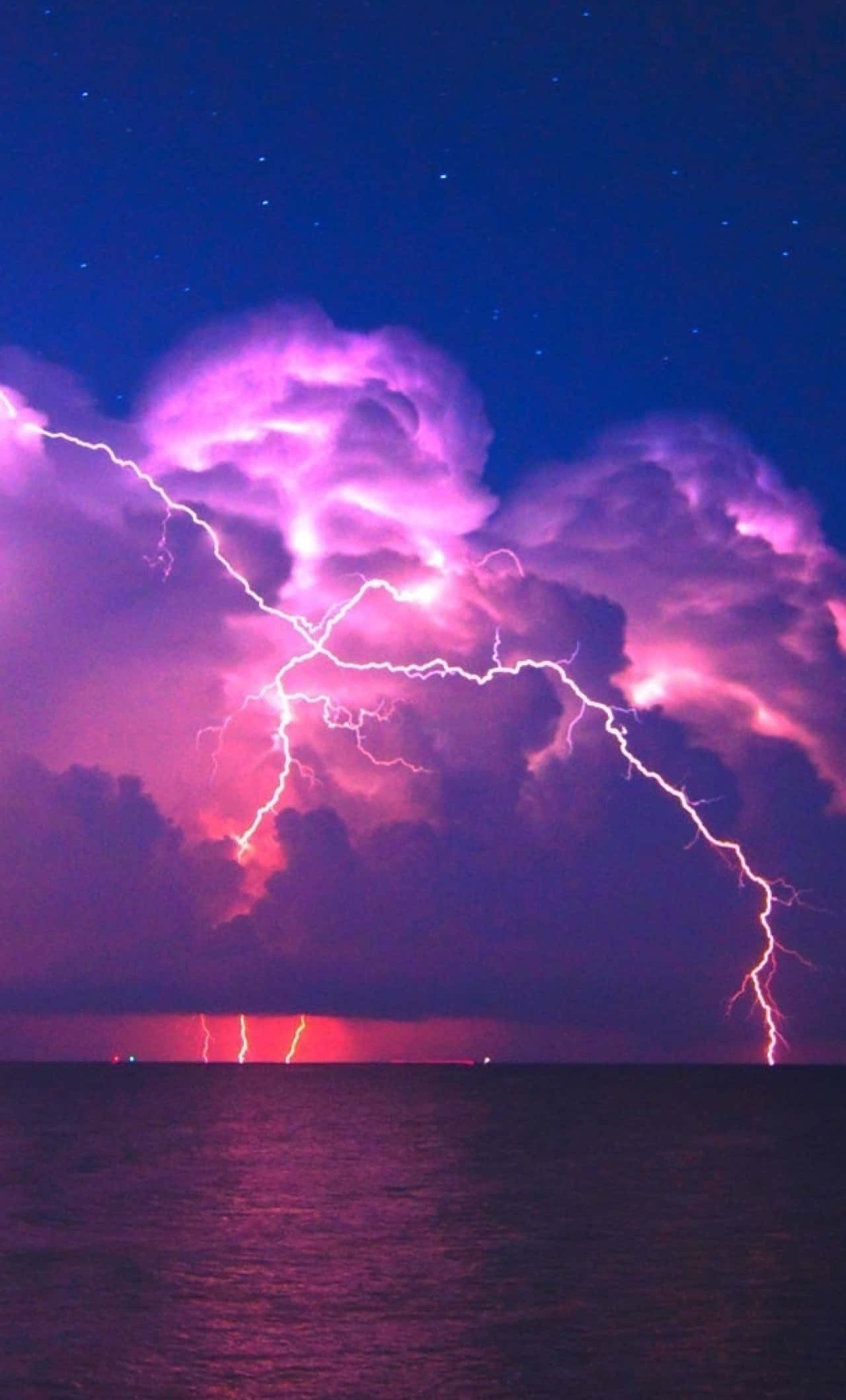 閃電 桌布 壁紙 — 鮮豔的紫色閃電在星夜下黑暗海洋上方的暴風雨天空中分叉。