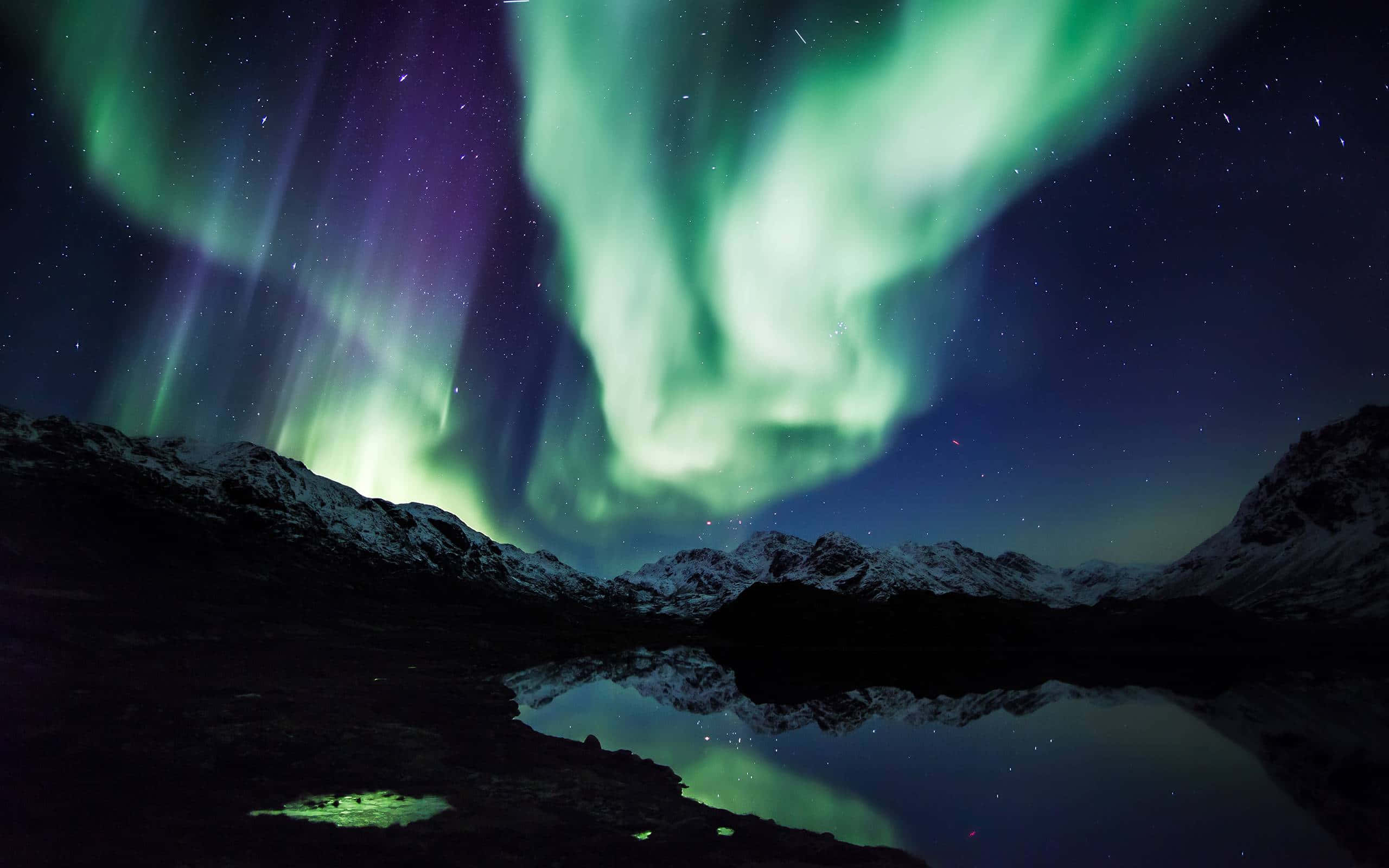 aurora borealis 桌布 壁紙 — 鮮豔的綠色和紫色北極光在星空下平靜的湖面倒映的雪山頂上舞動。