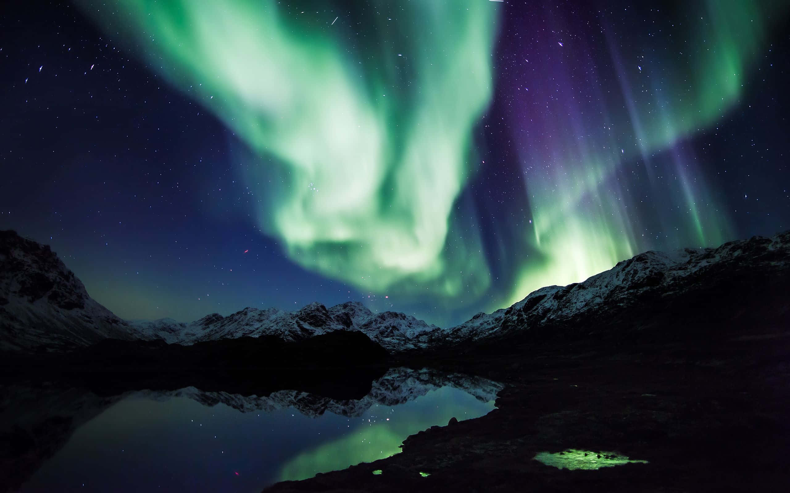 aurora borealis 桌布 壁紙 — 鮮豔的綠色和紫色北極光在星空下平靜的湖面倒映的雪山頂上舞動。