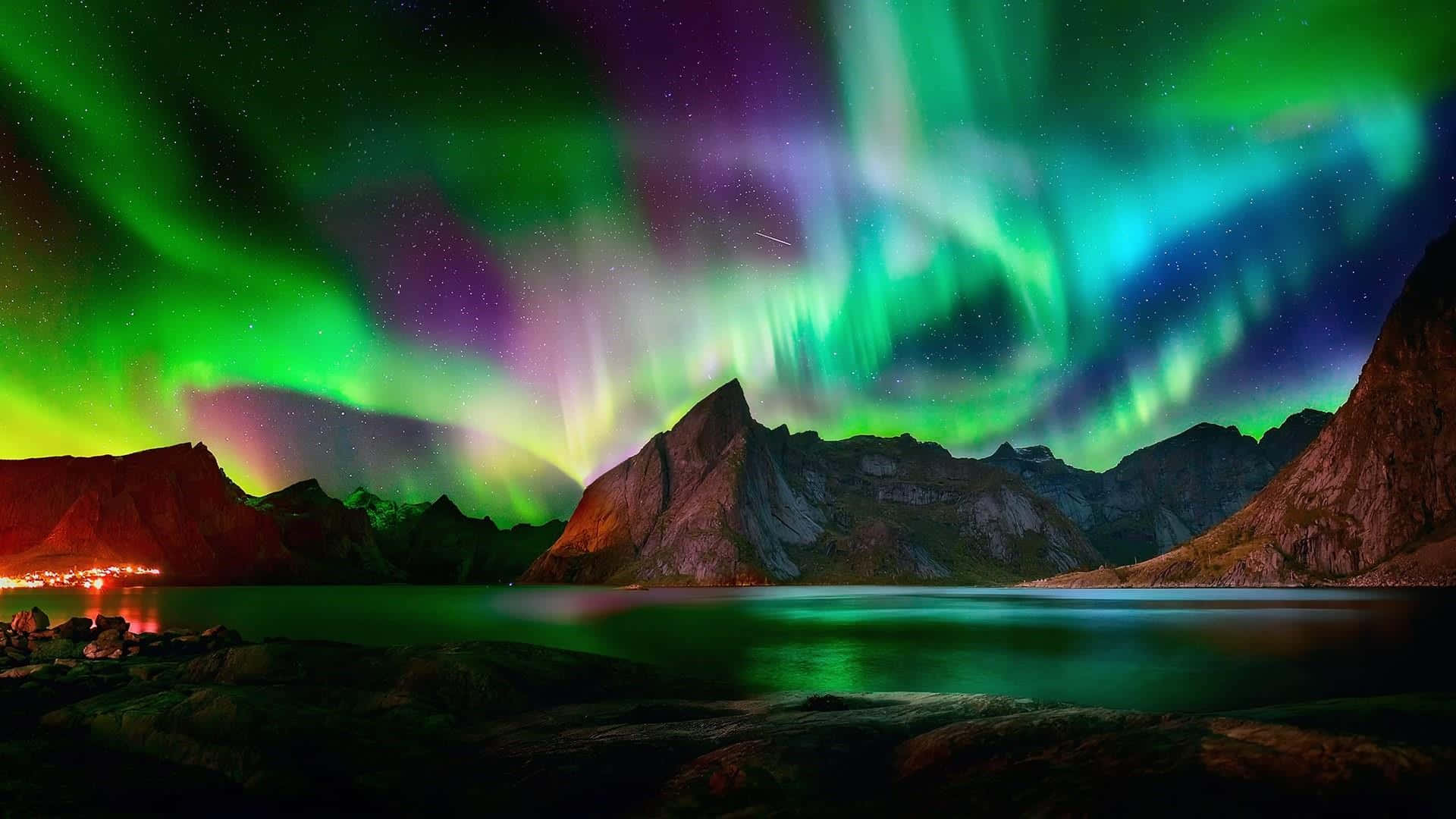 Aurora 桌布 壁紙 — 鮮豔的綠色和紫色極光在星夜下平靜的湖面上倒映的鋸齒狀山脈上方舞動。