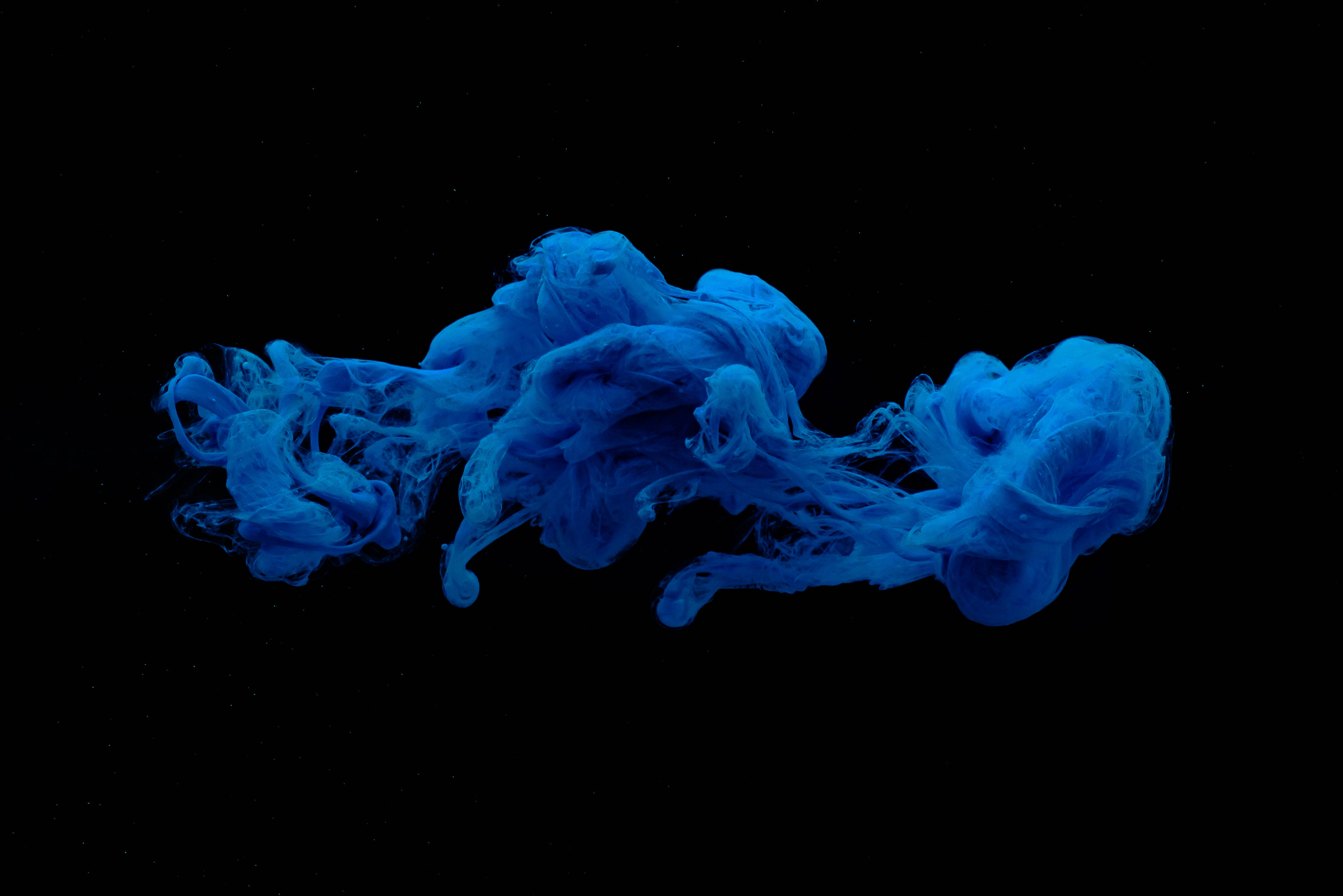 深藍色 桌布 壁紙 — 鮮豔的藍色墨水在純黑色背景上優雅地旋轉，營造出空靈的水下抽象運動。