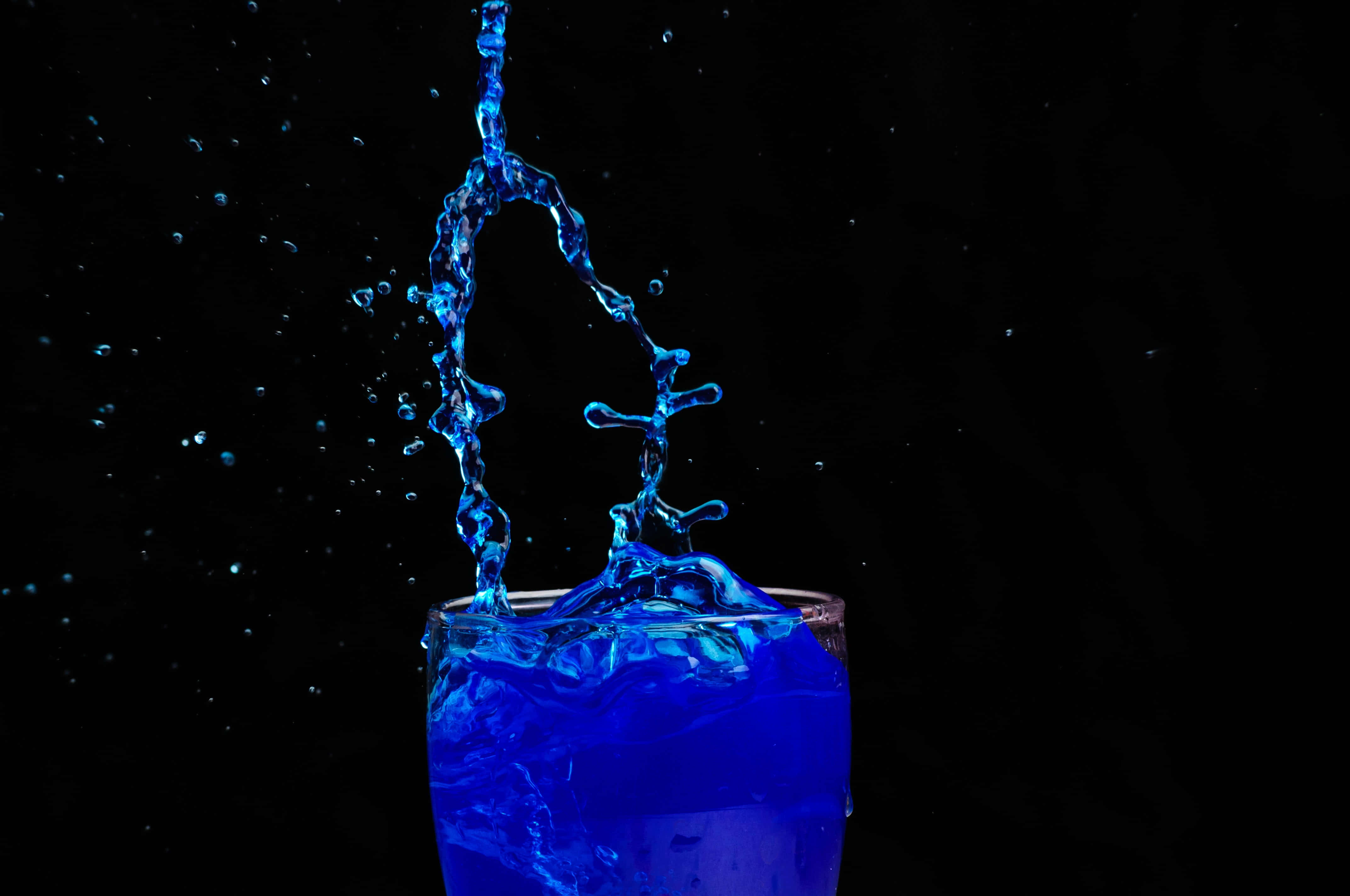 Liquid 桌布 壁紙 — 鮮豔的藍色液體從玻璃杯中戲劇性地向上飛濺，背景是純黑色。