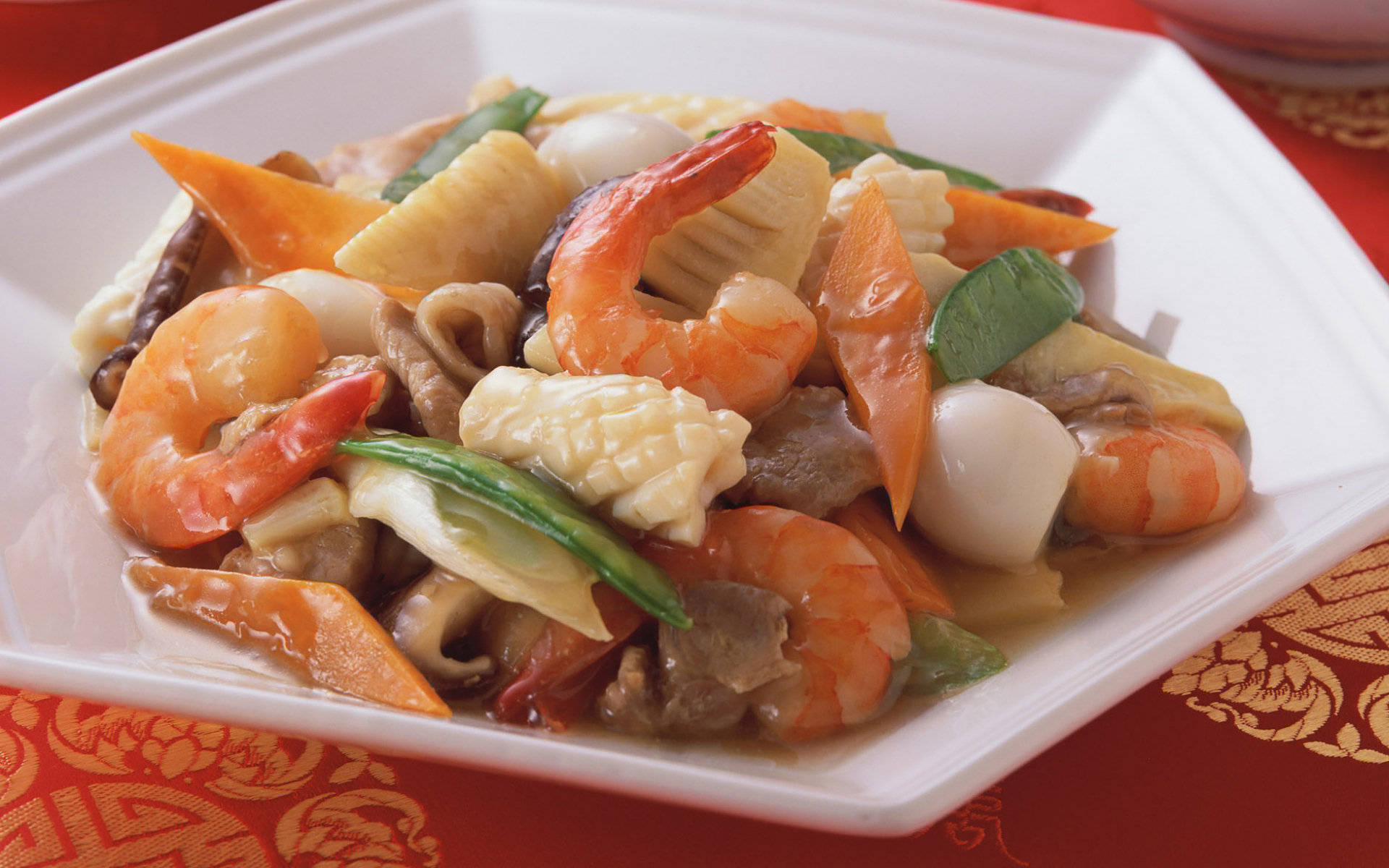 4K Food 桌布 壁紙 — 鮮豔的蝦、扇貝和蔬菜炒菜在紅色圖案桌布上的白色盤子中閃閃發光。