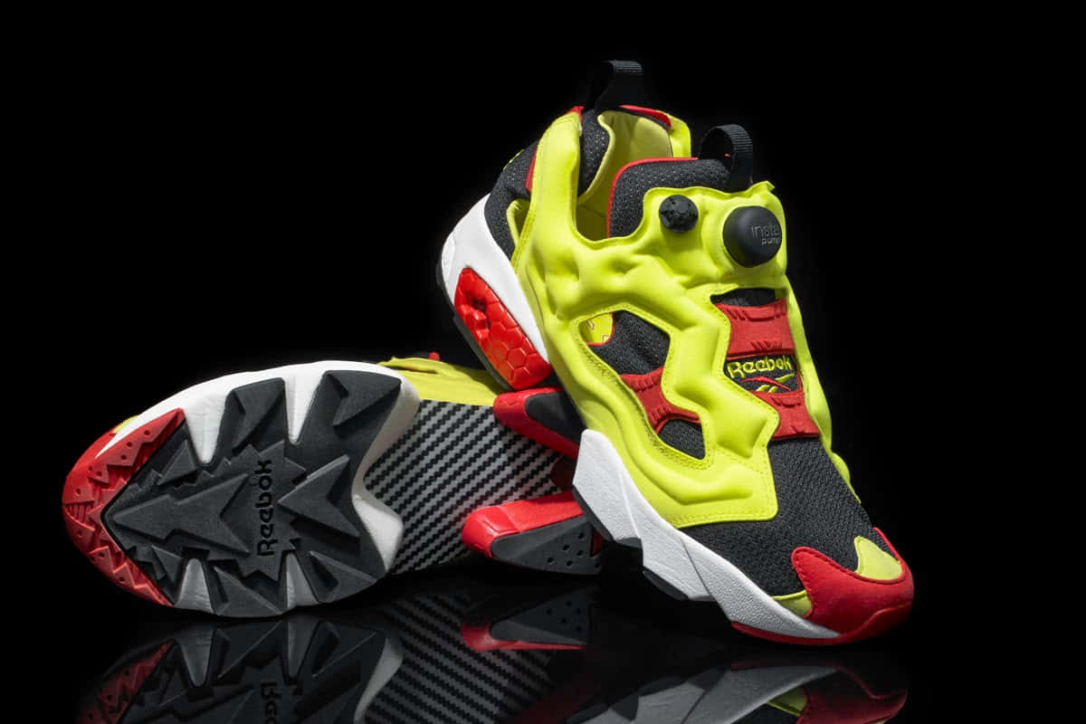 螢光黃、紅和黑色Reebok Pump運動鞋置於反射黑色表面上。 — Valorant Logo 壁紙