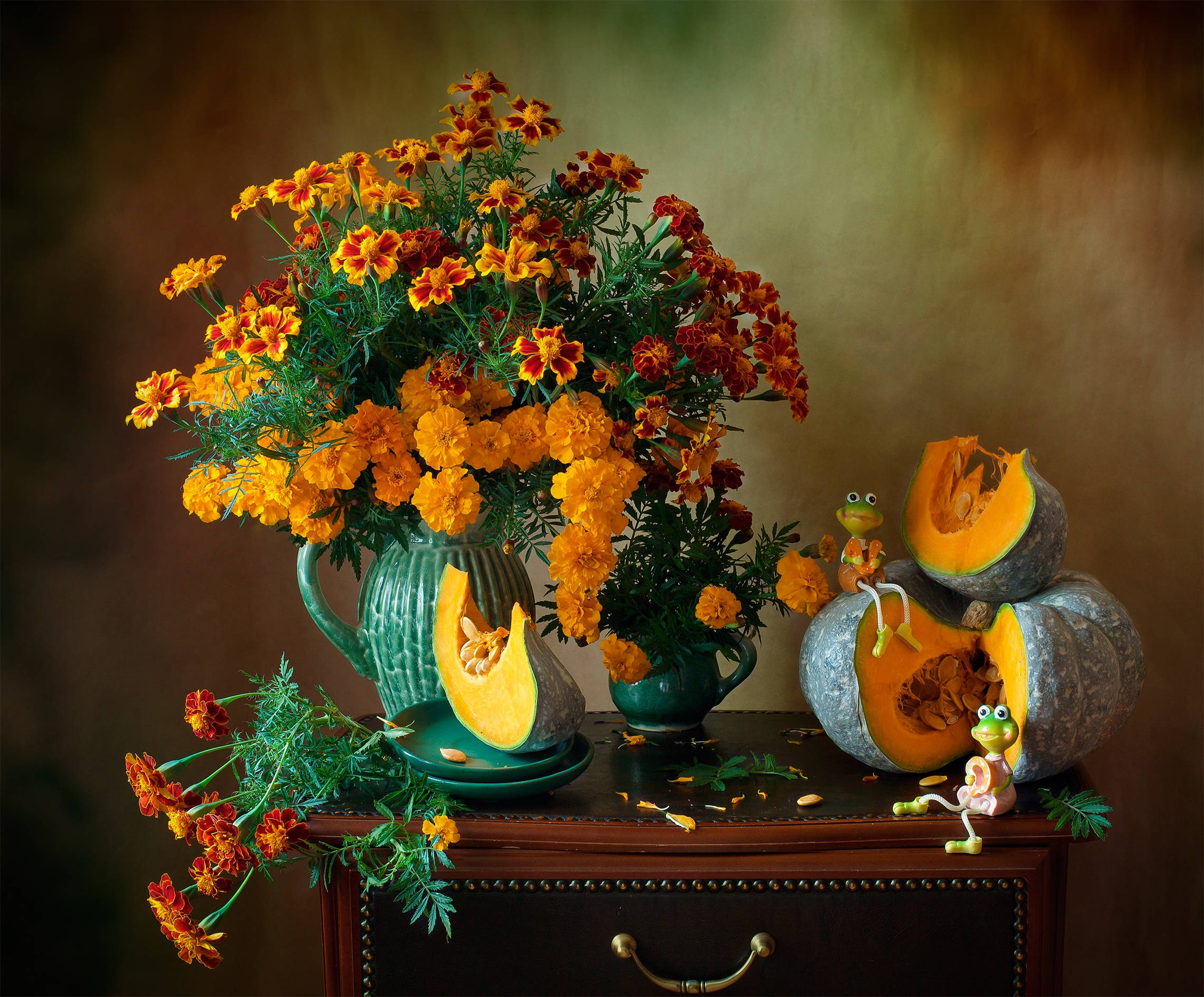 Marigold 桌布 壁紙 — 鮮豔的金盞花從藍綠色花瓶溢出，旁邊是雕刻南瓜和小青蛙，放在深色木製抽屜櫃上。
