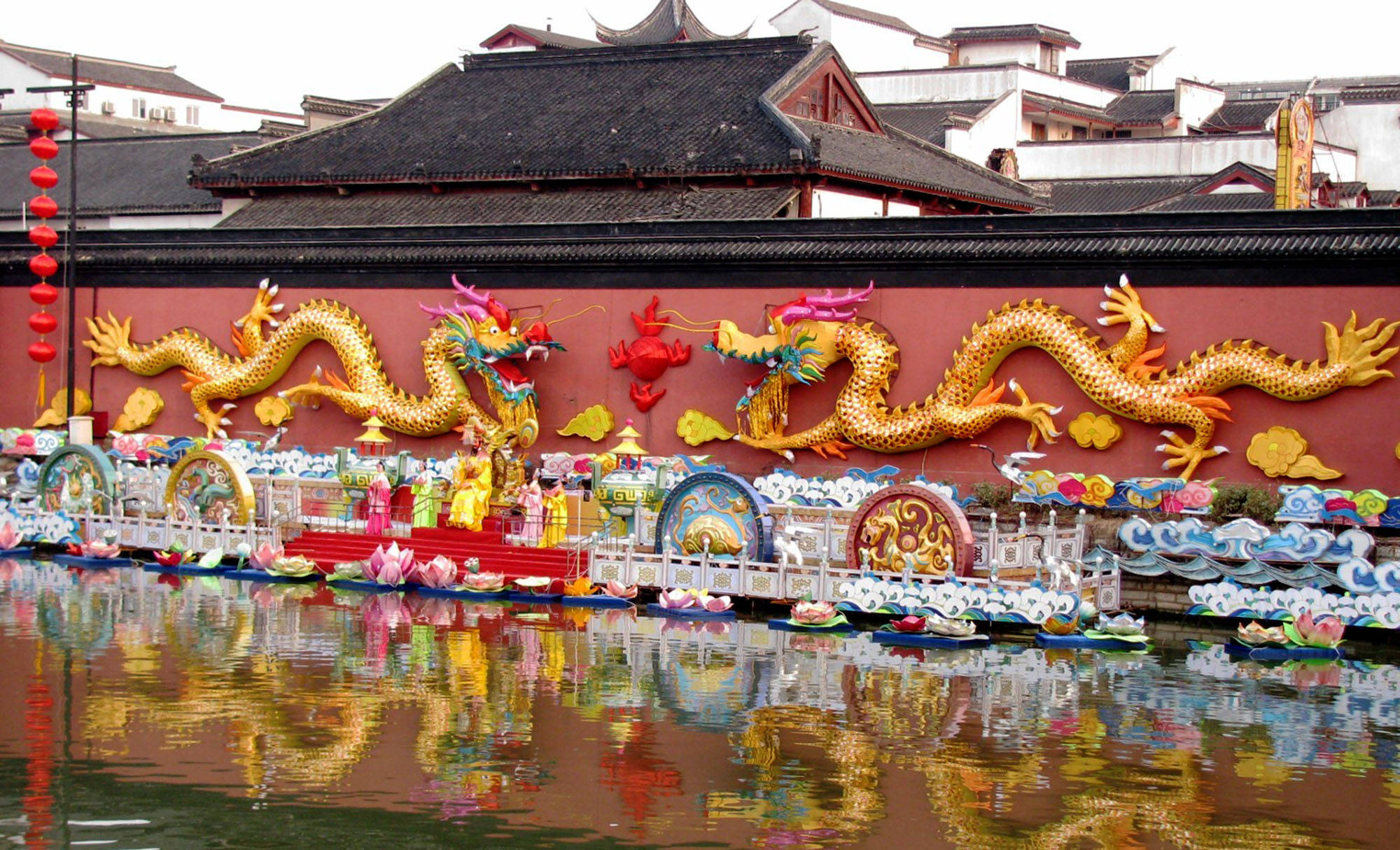 Nanjing 桌布 壁紙 — 鮮豔的金龍裝飾在紅牆上，下方是色彩繽紛的船隻和燈籠在平靜水面上倒影的節日水上遊行。