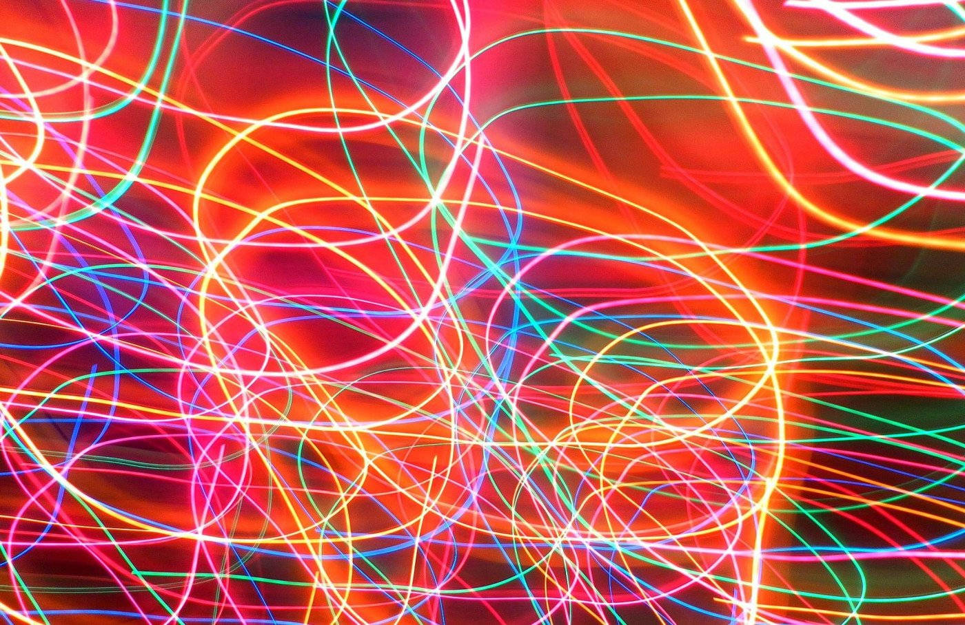 Neon Light 桌布 壁紙 — 鮮豔的霓虹燈光軌跡在火紅背景上以混亂圖案旋轉，營造出充滿活力的抽象光芒。