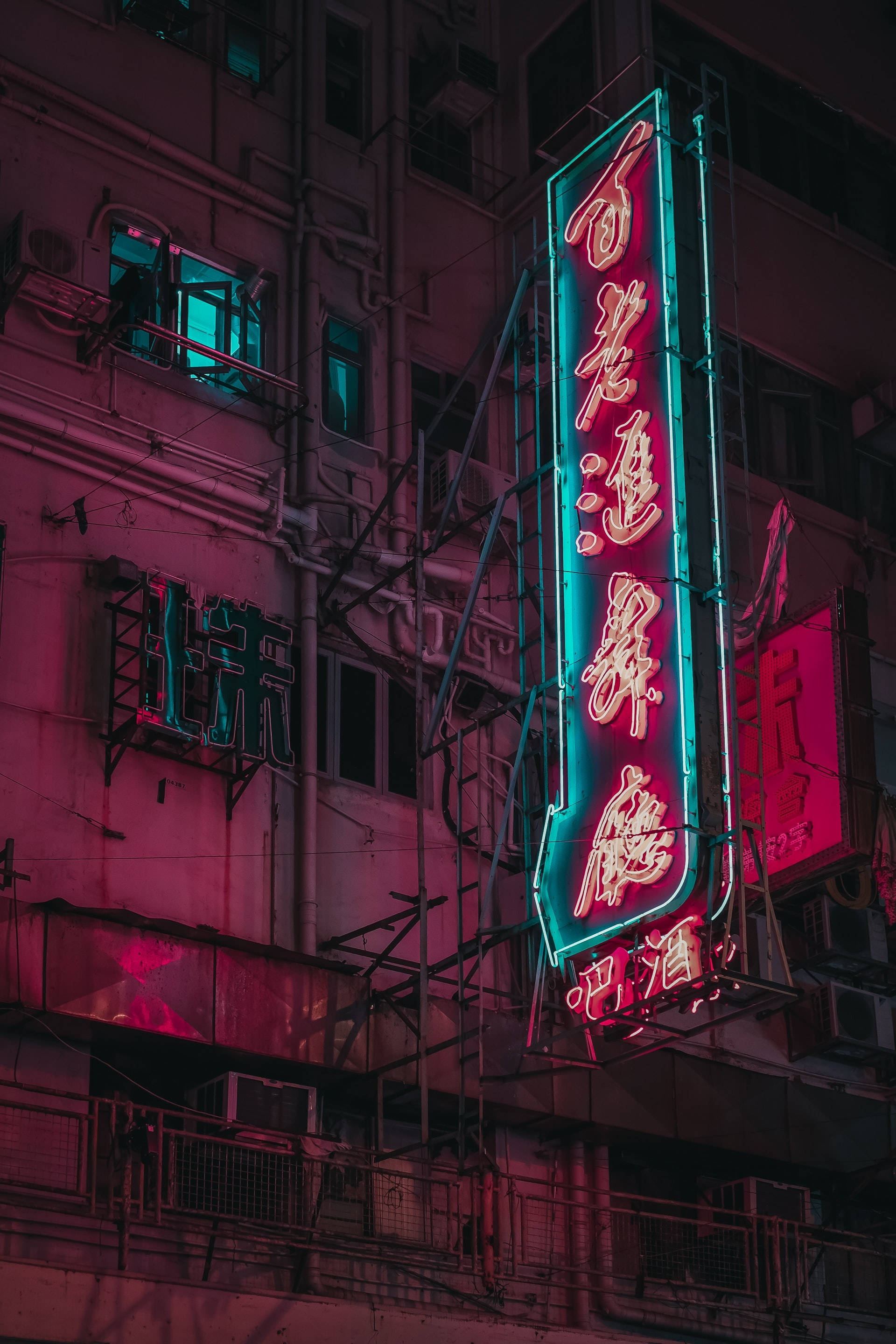 neon sign 桌布 壁紙 — 鮮豔的霓虹燈在夜間對著風化的城市建築外牆發出粉紅色和藍綠色的光芒。