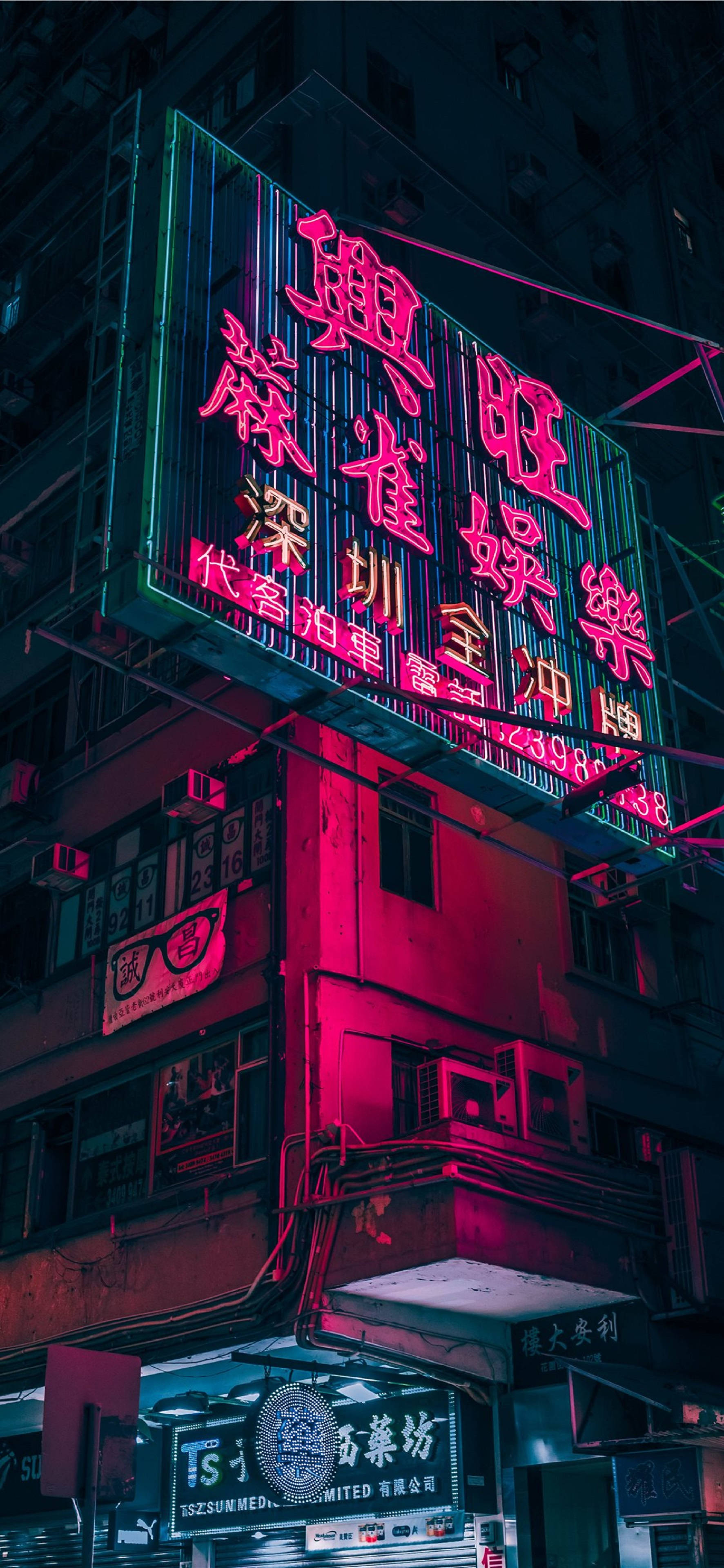 4K 霓虹 iPhone 桌布 壁紙 — 鮮豔的霓虹燈在夜間對著黑暗的城市建築外牆發出粉紅色和綠色的光芒。