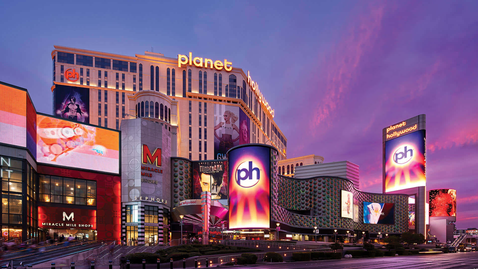 好萊塢 桌布 壁紙 — 鮮豔的霓虹燈招牌照亮了 Planet Hollywood 度假村，背景是帶有粉紅色和紫色雲彩的暮色天空。
