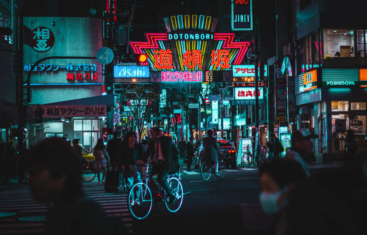 夜晚 桌布 壁紙 — 鮮豔的霓虹燈照亮了夜晚繁忙的東京街道，騎自行車者和行人穿梭在發光的都市峽谷中。