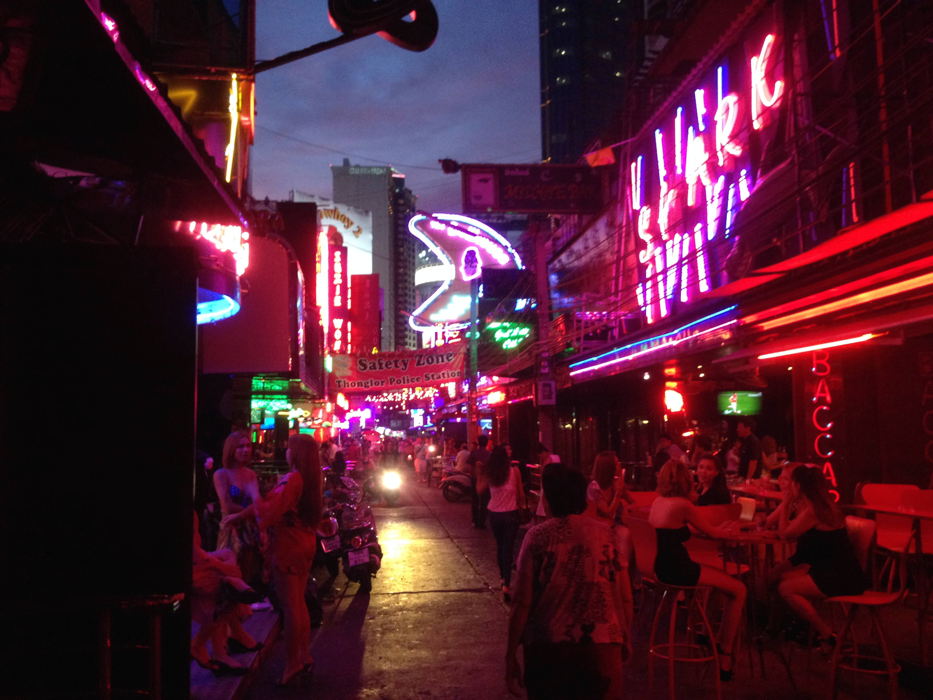 Bangkok 桌布 壁紙 — 鮮豔的霓虹燈照亮了黃昏時分繁忙的城市小巷，人們在閃爍的紅色和粉紅色燈光下社交和用餐。