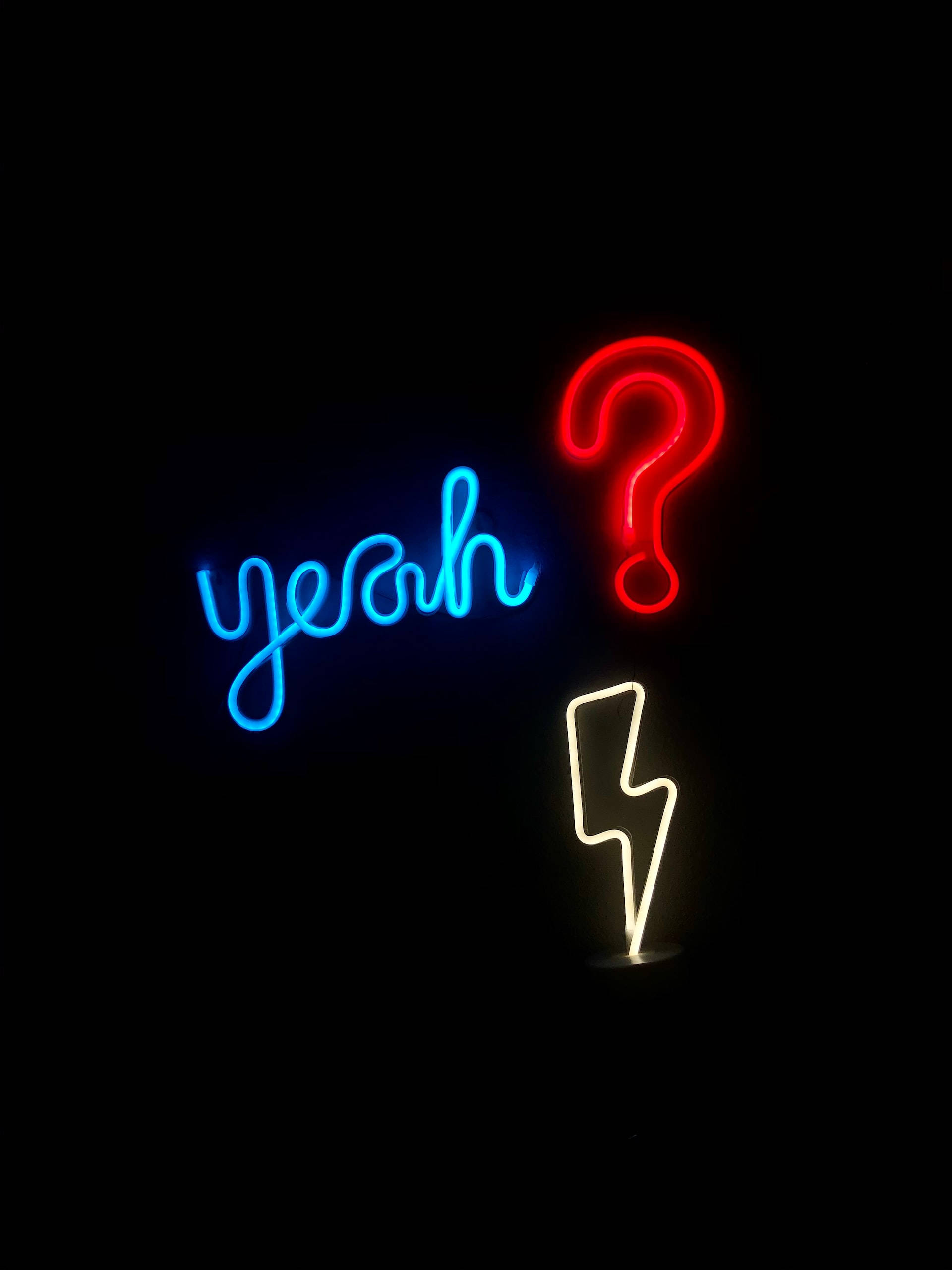 Lightning Bolt iPhone 桌布 壁紙 — 鮮豔的霓虹燈牌在漆黑背景上發出藍色 yeah、紅色問號和白色閃電的光芒。
