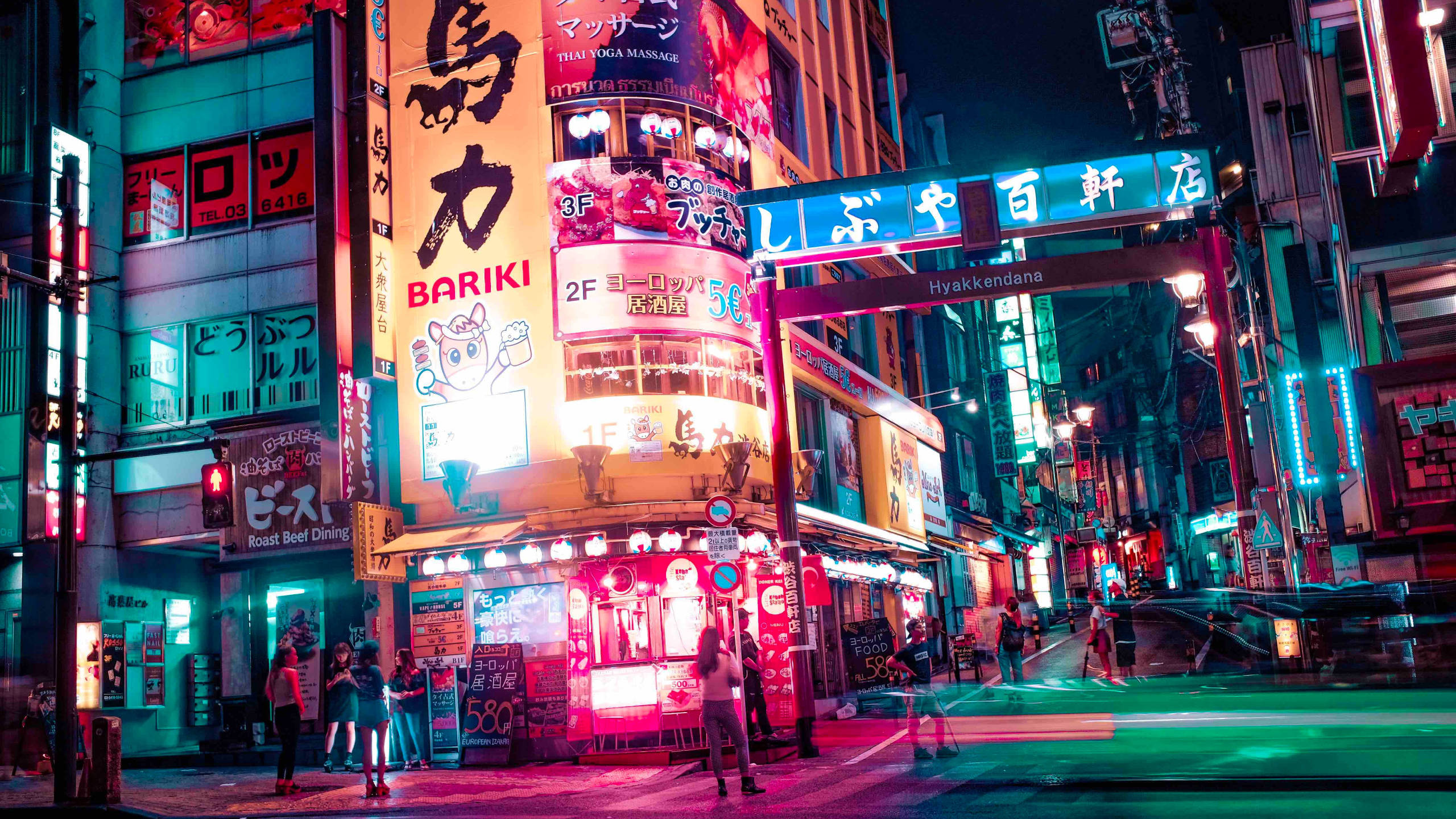 日本 桌布 壁紙 — 鮮豔的霓虹燈牌照亮了夜晚繁忙的東京街道，粉紅色、綠色和藍色的燈光在潮濕的人行道上反射。
