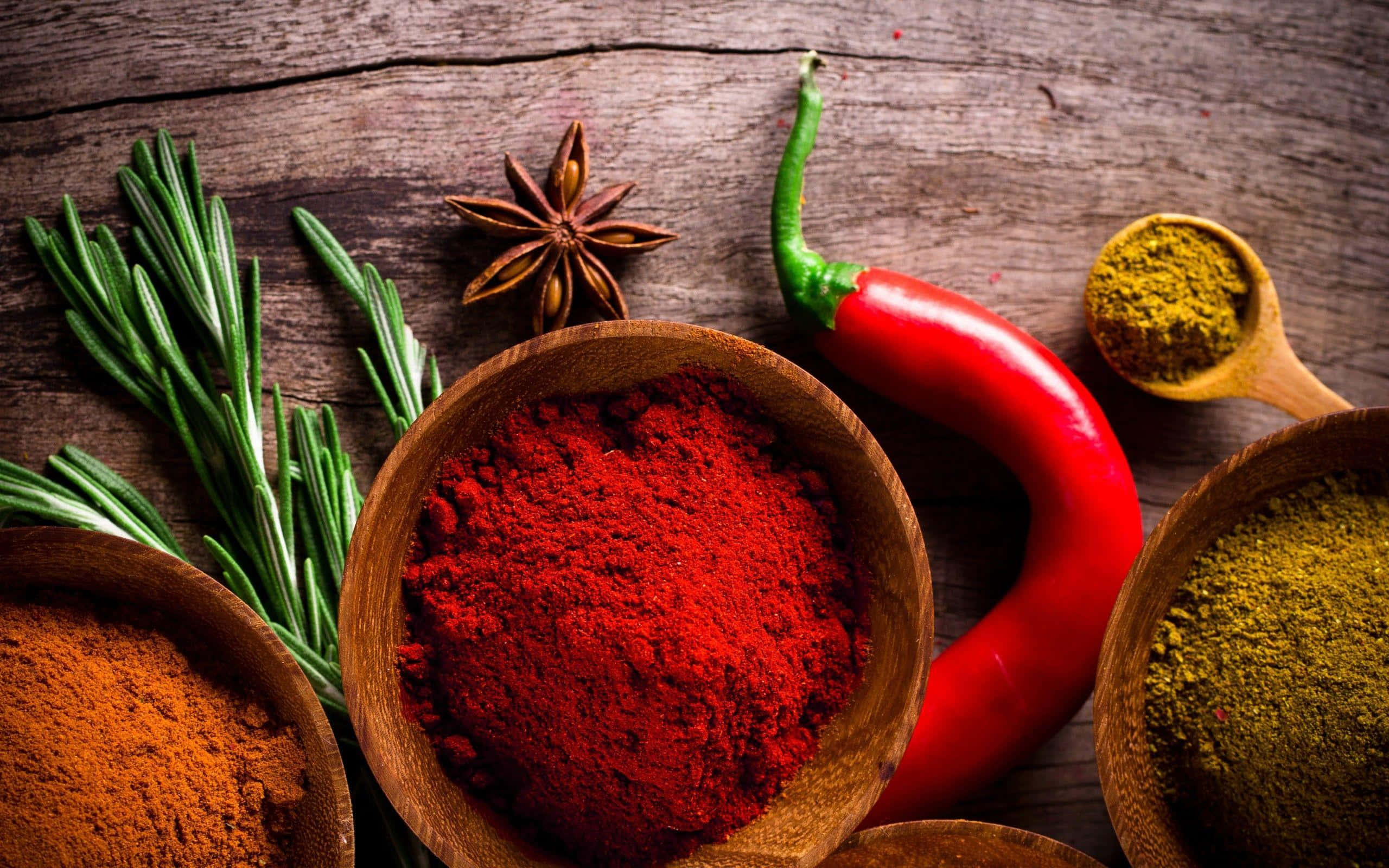 Spices 桌布 壁紙 — 鮮豔的香料和香草，如紅辣椒粉、迷迭香和八角，排列在質樸的木質表面上。