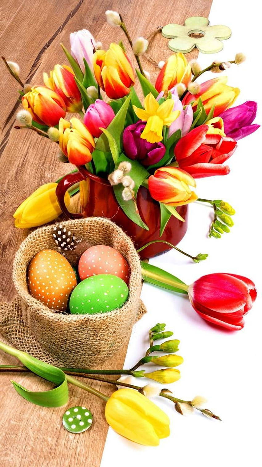 Easter Phone 桌布 壁紙 — 鮮豔的鬱金香和帶圖案的復活節蛋擺放在木質表面上的質樸黃麻籃子裡。