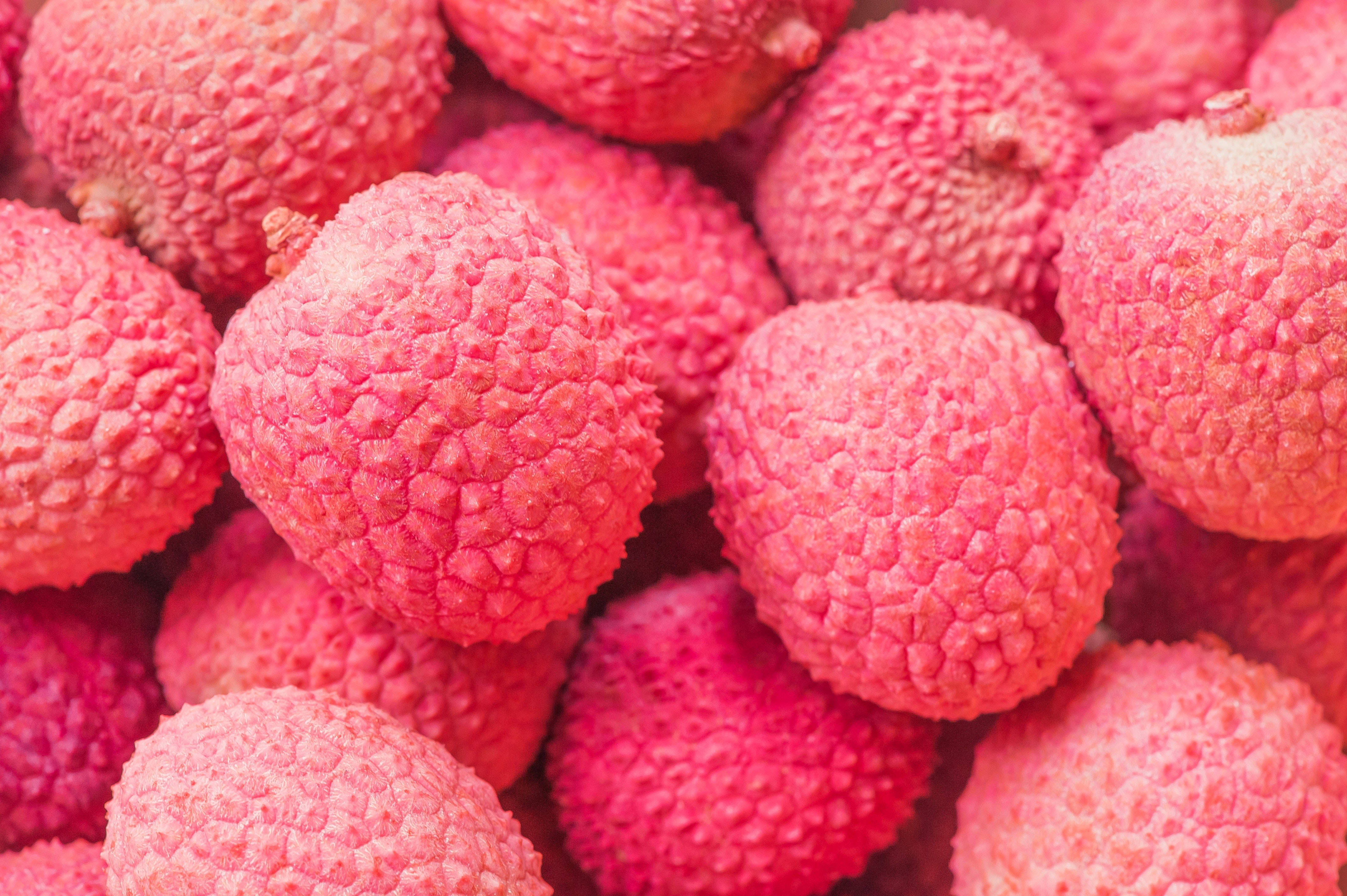 Litchi 桌布 壁紙 — 鮮豔粉紅色荔枝的特寫，表面凹凸不平、有紋理，堆疊在一起。