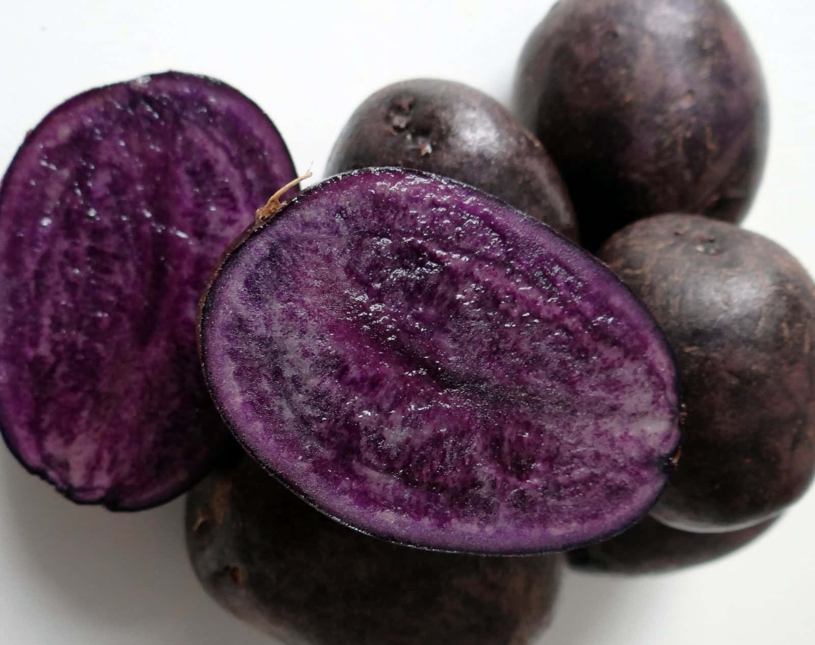Purple Potato 桌布 壁紙 — 鮮豔紫色馬鈴薯的特寫，內部果肉豐富，粗糙的深色外皮，背景為純白色。