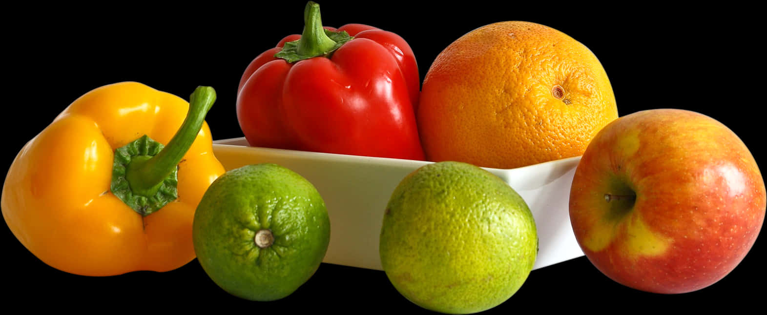 Fruits And Vegetables 桌布 壁紙 — 鮮黃色、紅色和綠色的燈籠椒、萊姆和一個橙色的蘋果，排列在一個白色碗中，背景為純黑色。