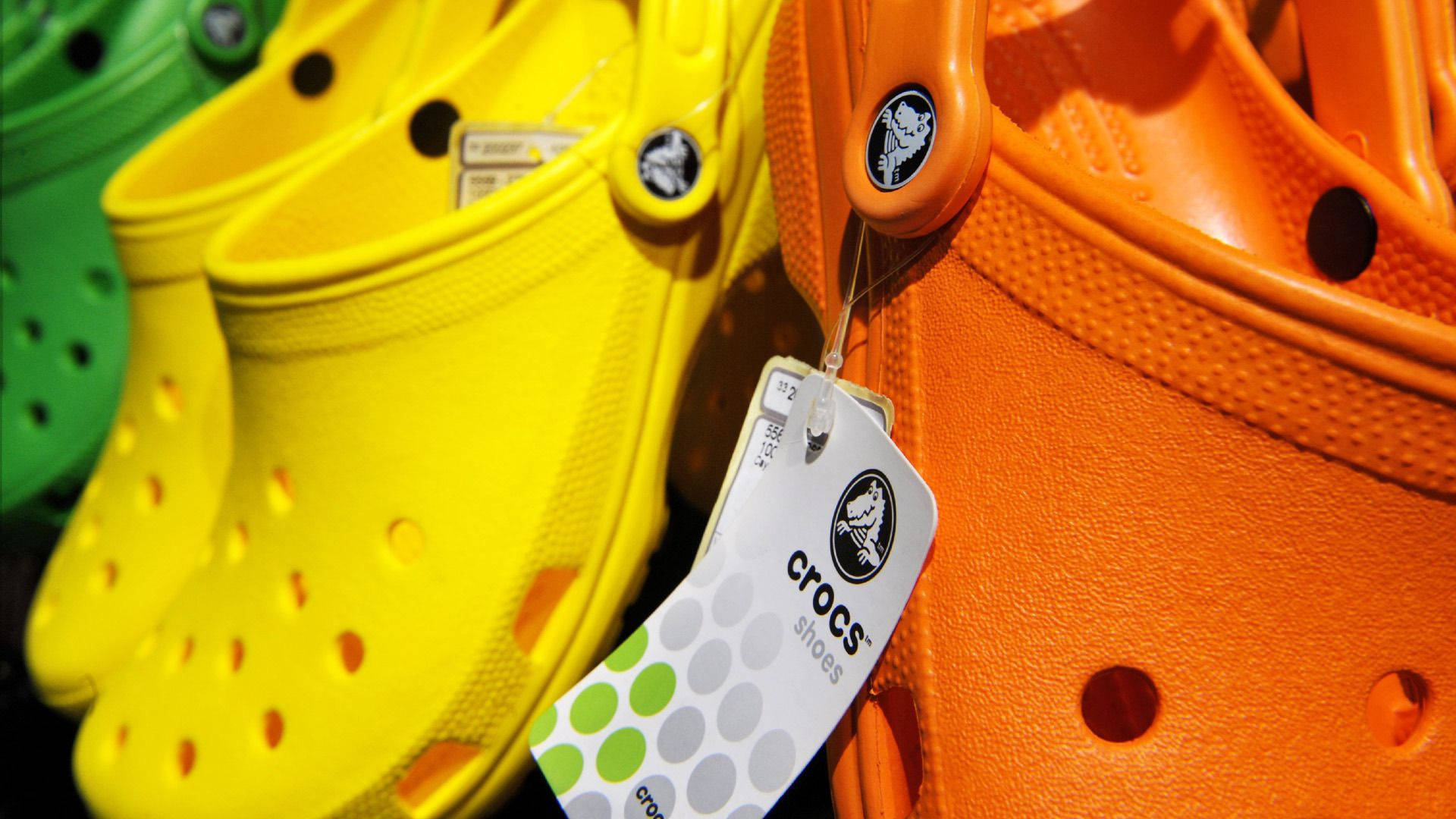 Crocs 桌布 壁紙 — 鮮黃色和橙色Crocs鞋，帶有品牌標籤的零售特寫照。