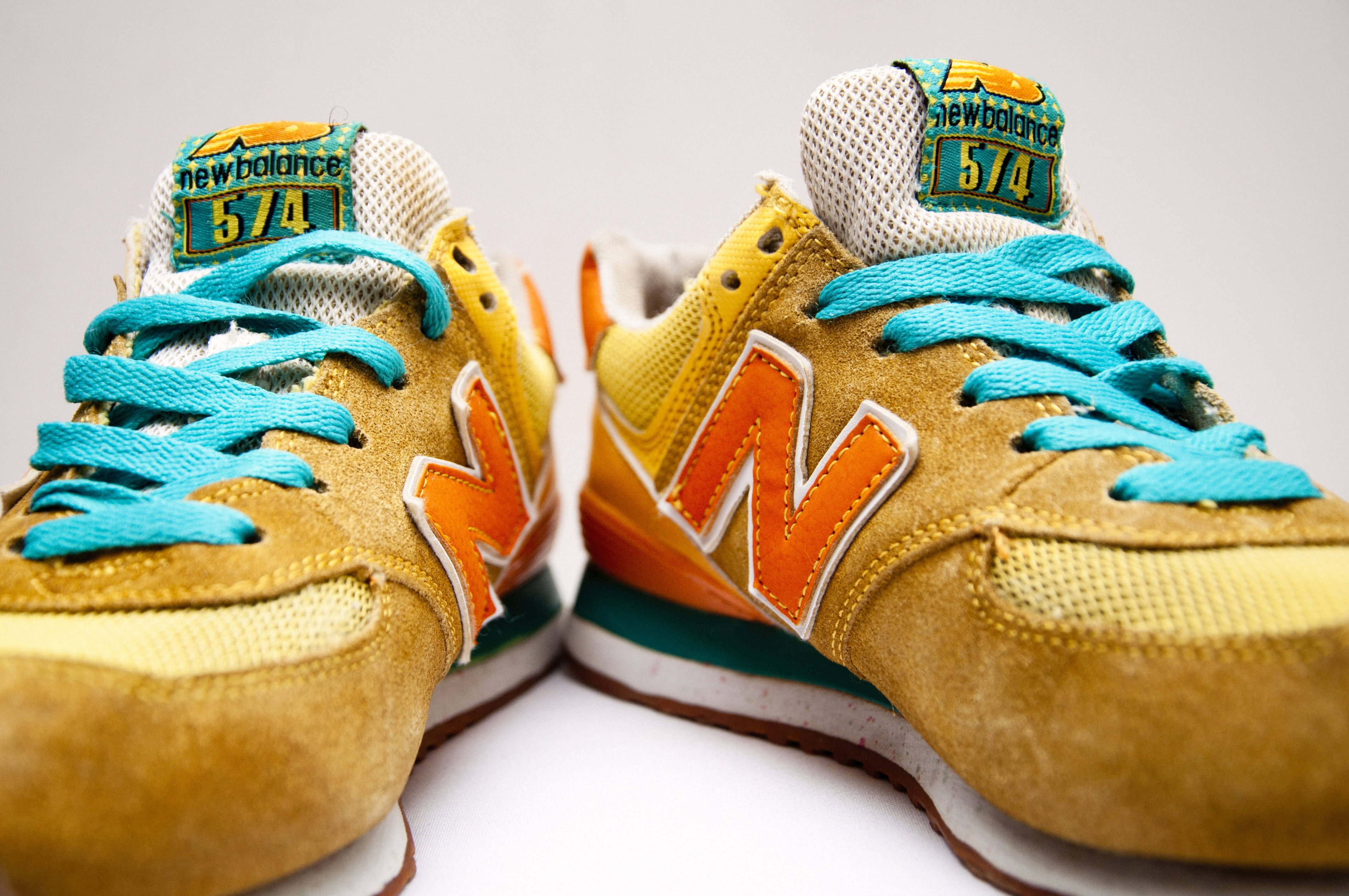 New 桌布 壁紙 — 鮮黃色和橙色New Balance 574運動鞋的特寫，配有藍綠色鞋帶，背景為純白色。