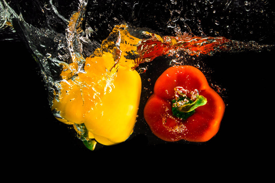 Fruits 桌布 壁紙 — 鮮黃色和紅色的甜椒在水中碰撞，在黑色背景上產生爆炸性的水花。