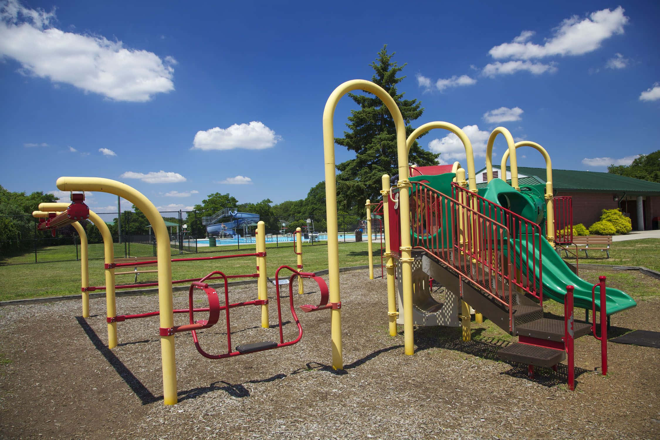 Playground 桌布 壁紙 — 鮮黃色和紅色的遊樂場設備矗立在明亮的藍天下，伴隨著蓬鬆的白雲。