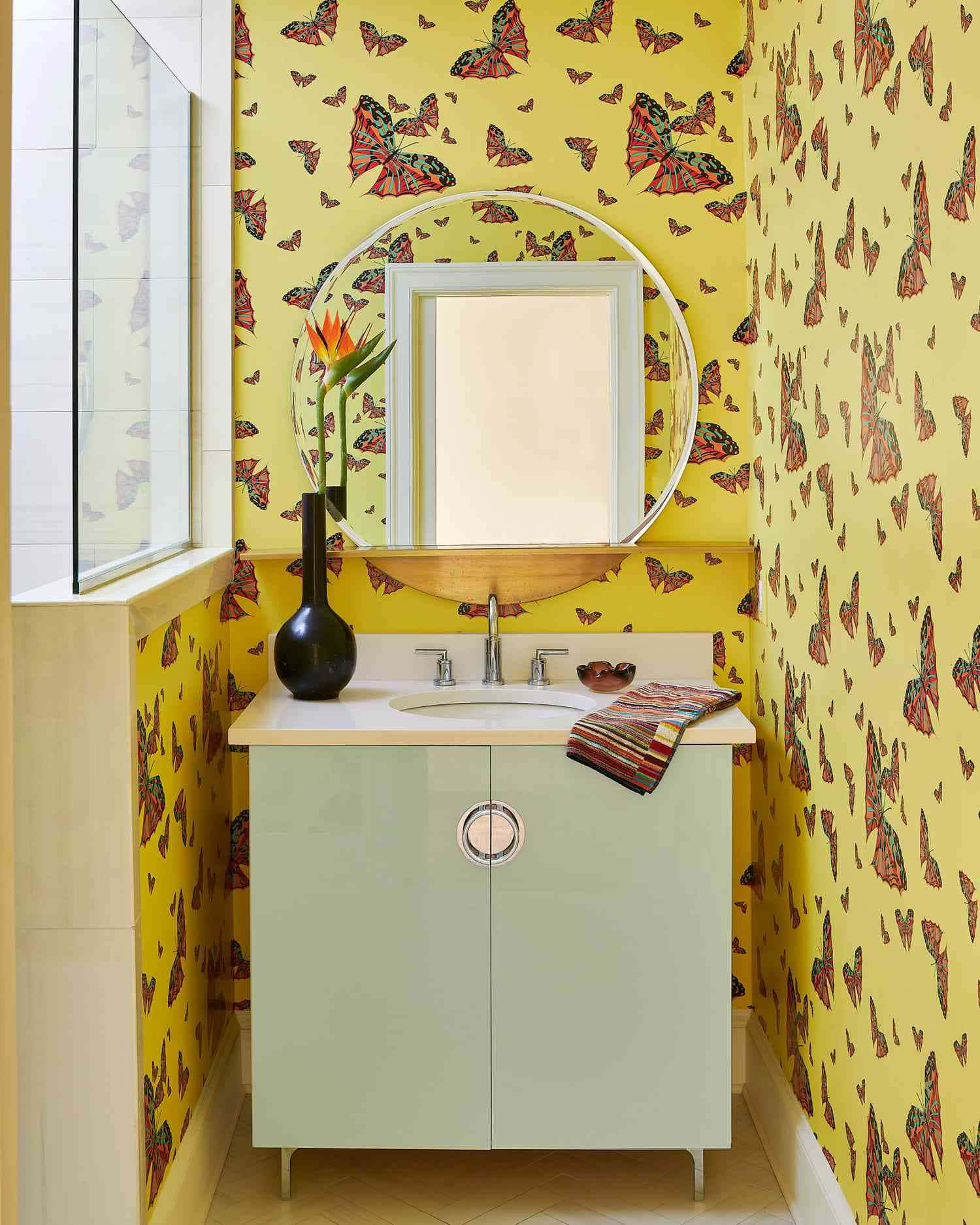 Bathroom Decor 桌布 壁紙 — 鮮黃色壁紙飾有紅色和黑色蝴蝶，框住一個薄荷綠色的梳妝台，配有圓形鏡子和熱帶花瓶。