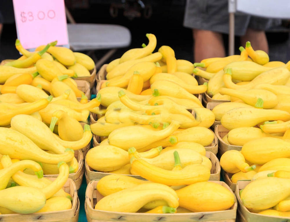 Fruits And Vegetables 桌布 壁紙 — 鮮黃色夏季南瓜堆疊在編織籃中，位於熱鬧的農夫市集攤位。