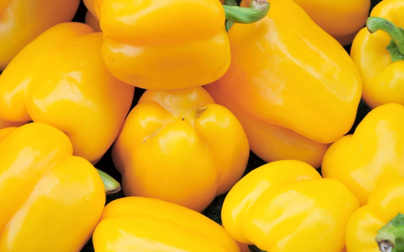 Yellow Bell Pepper 桌布 壁紙 — 鮮黃色甜椒與綠色莖部堆疊在一起的鮮明特寫。