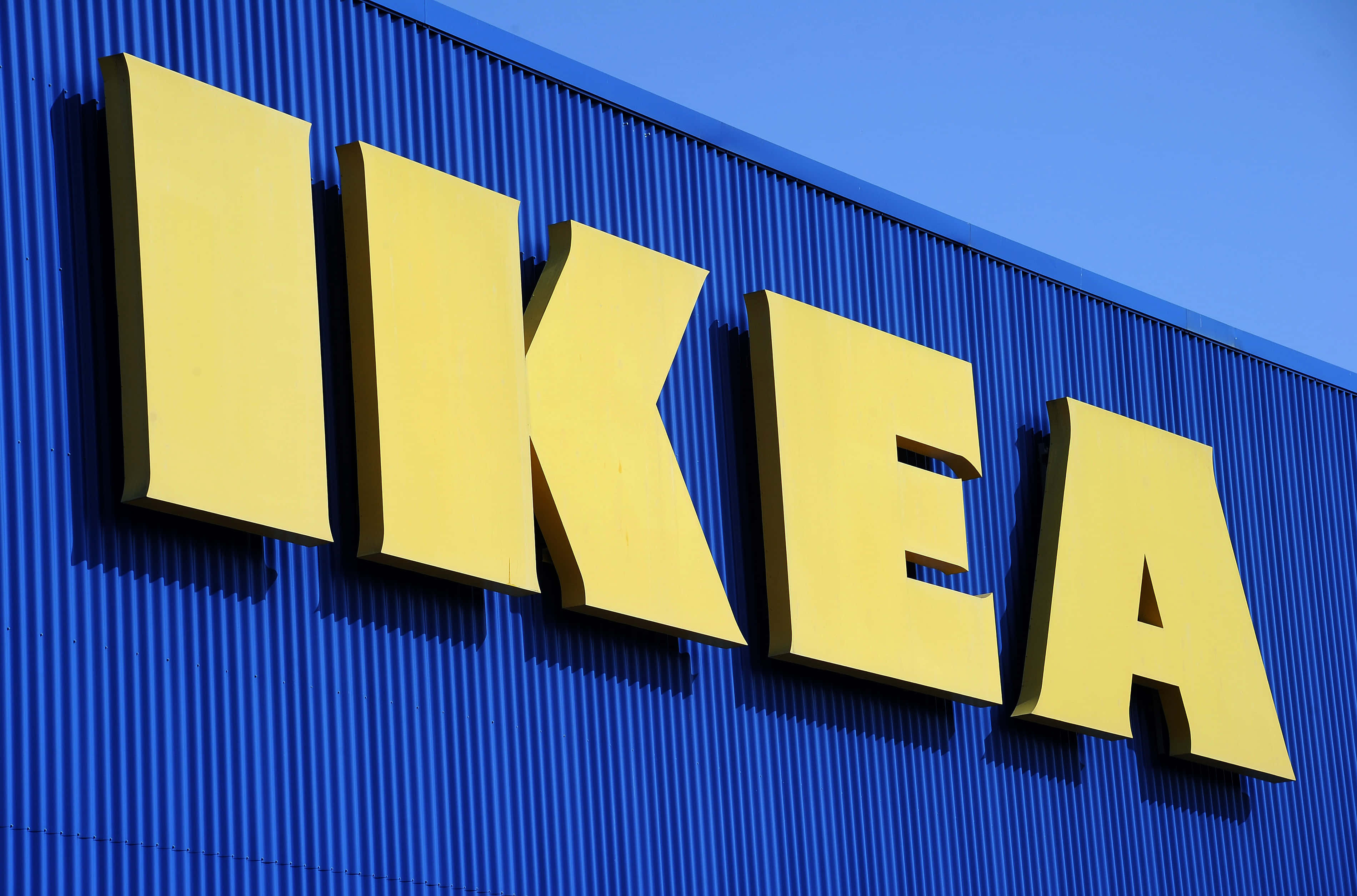 Ikea 桌布 壁紙 — 鮮黃色的IKEA字母在晴朗天空下，於充滿活力的藍色波紋金屬店面外牆上格外突出。