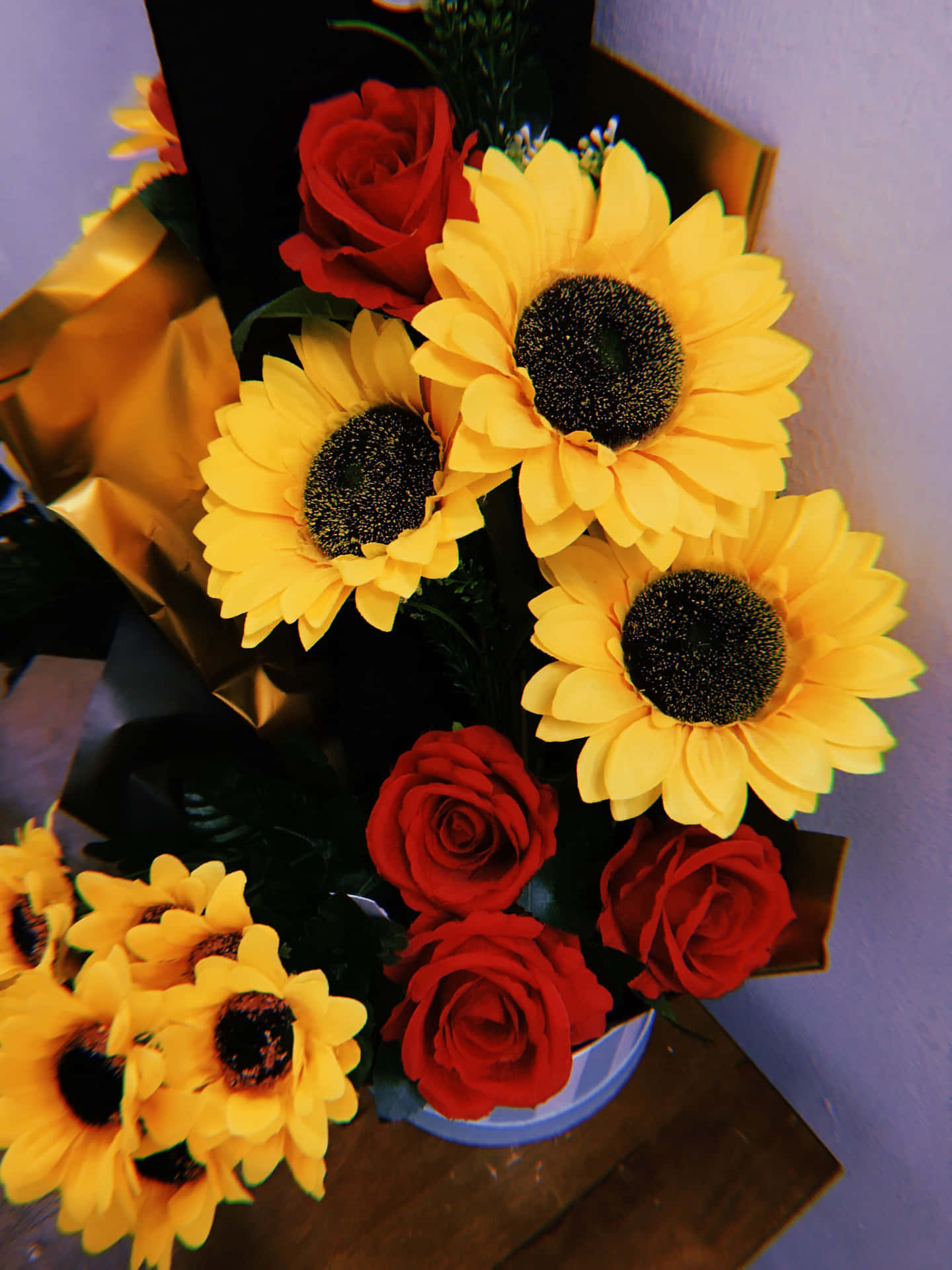 Roses 桌布 壁紙 — 鮮黃色的向日葵和深紅色的玫瑰，以金色包裝的藍色花瓶插在木質表面上。