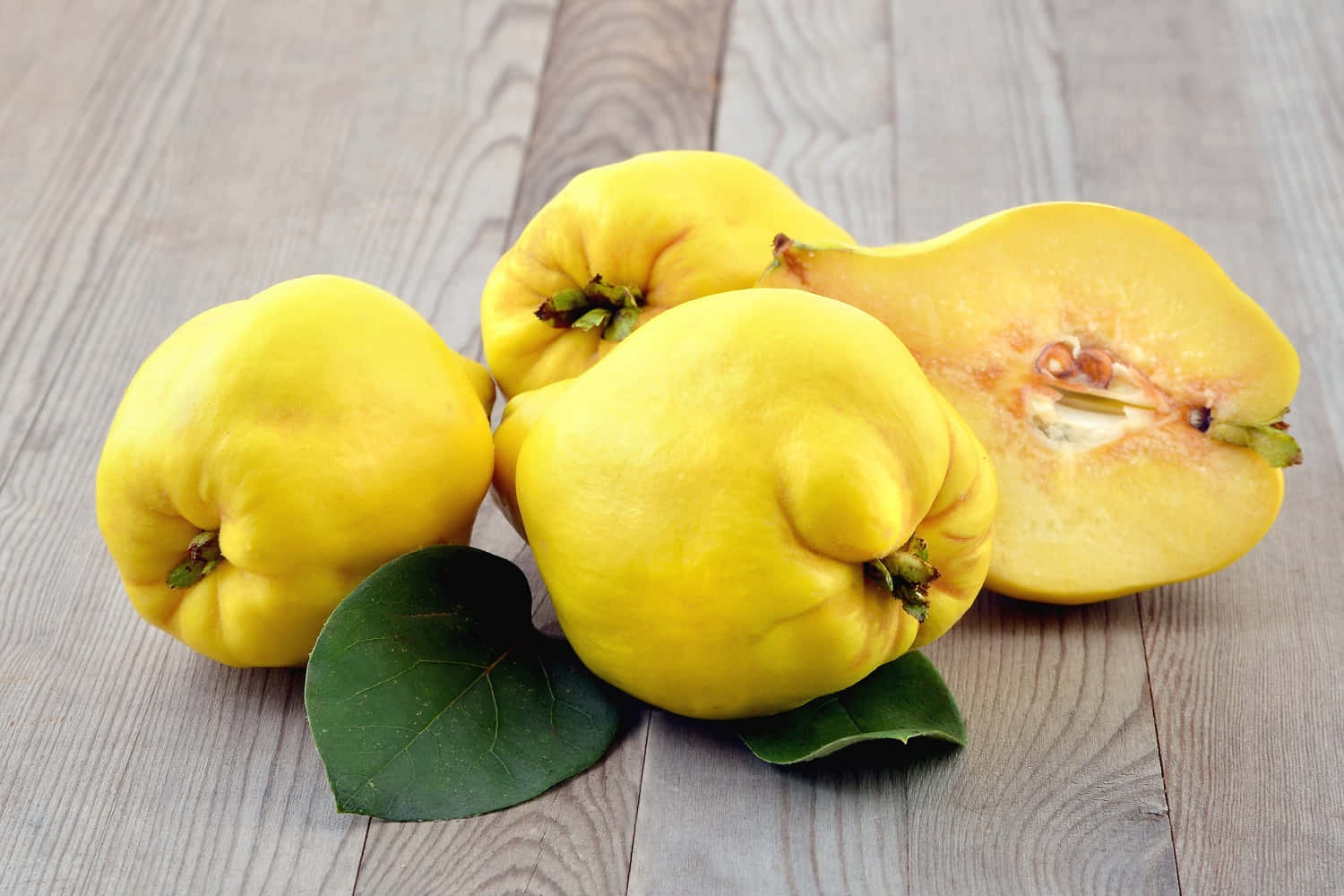 Quince 桌布 壁紙 — 鮮黃色的榲桲，其中一個切開露出淡色果肉和種子，放在經風化的木板上，配以深綠色葉子。