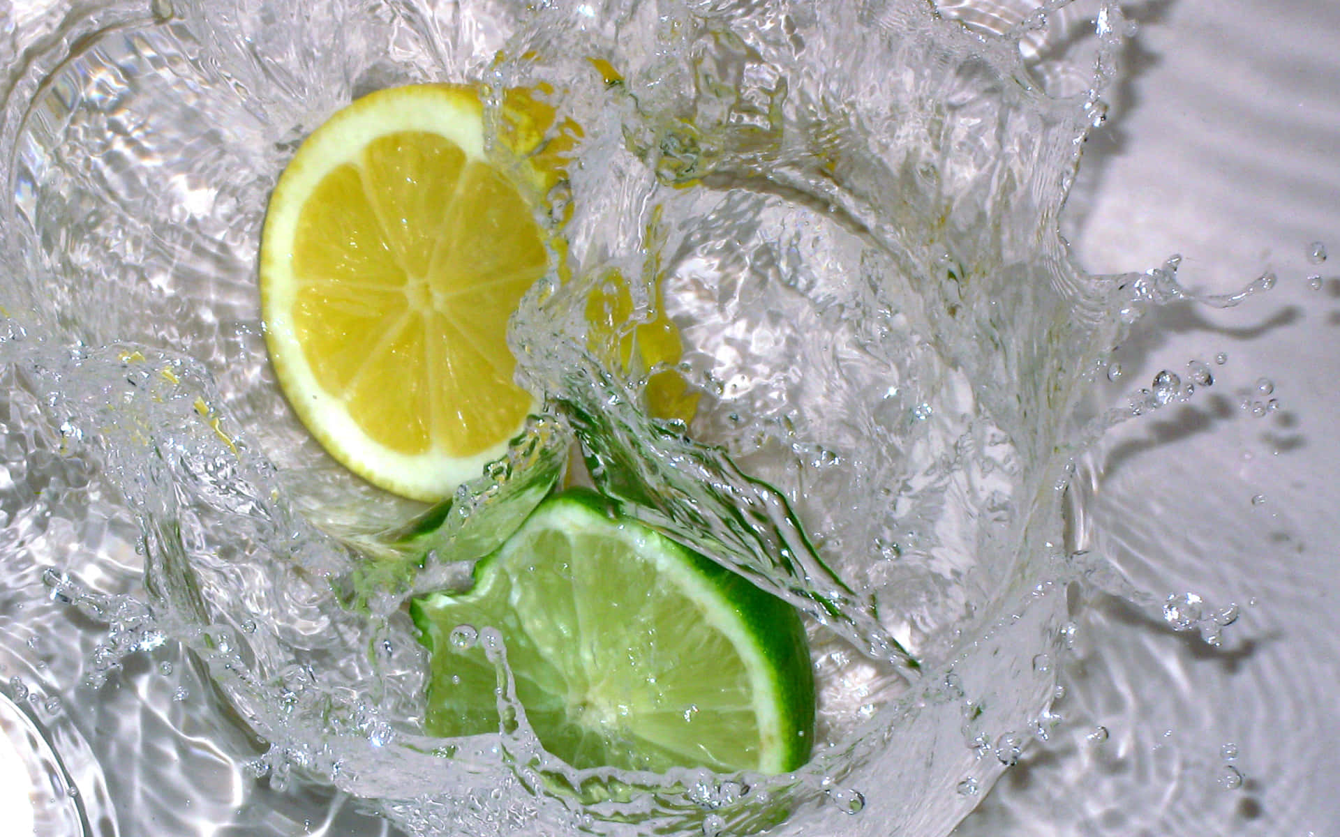 Refreshing 桌布 壁紙 — 鮮黃色的檸檬和青綠色的萊姆片在清澈的水中濺起動態水花，伴隨著閃閃發光的水滴。