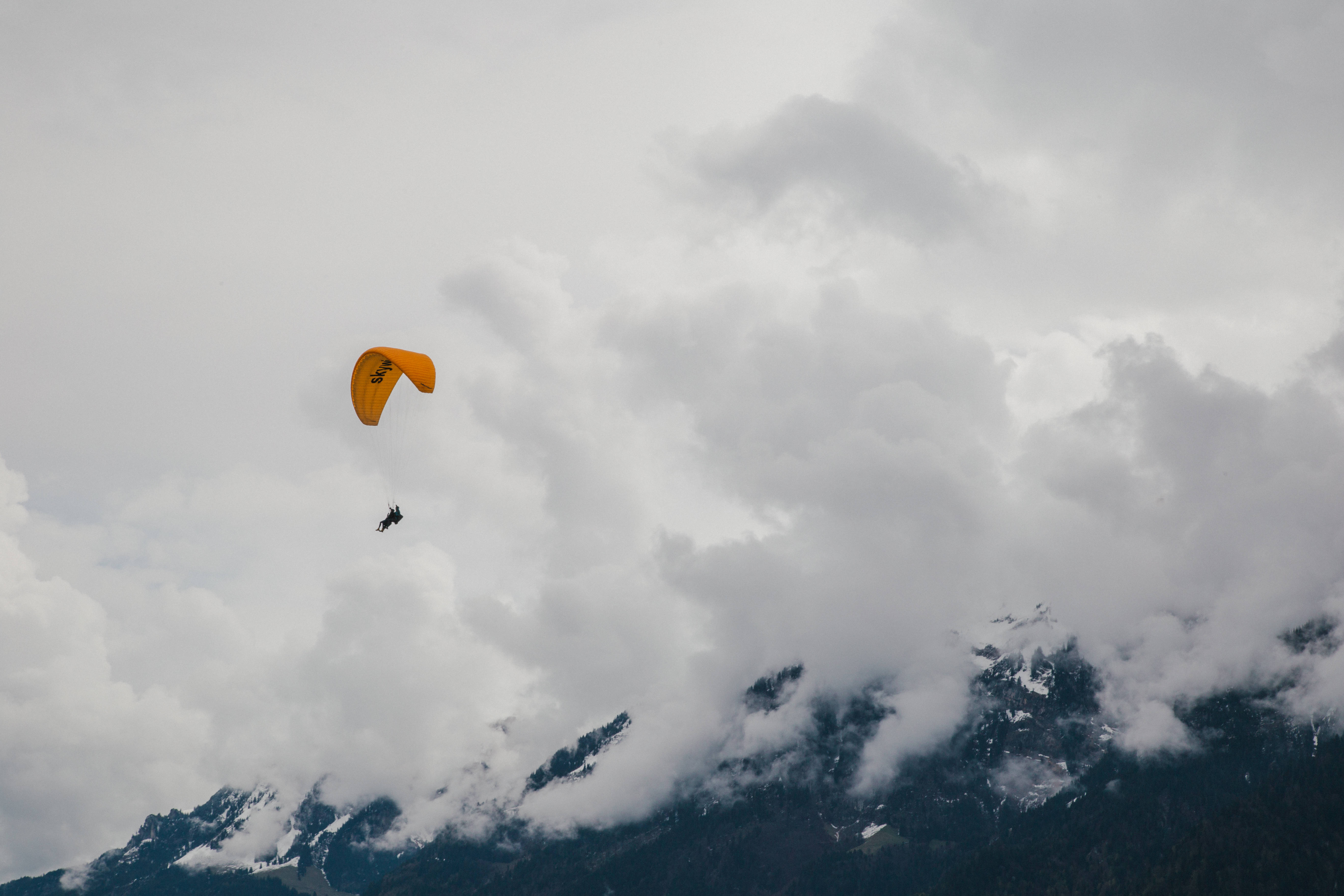 Paragliding 桌布 壁紙 — 鮮黃色的滑翔傘在部分被厚厚白雲遮蓋的雪山之上翱翔。