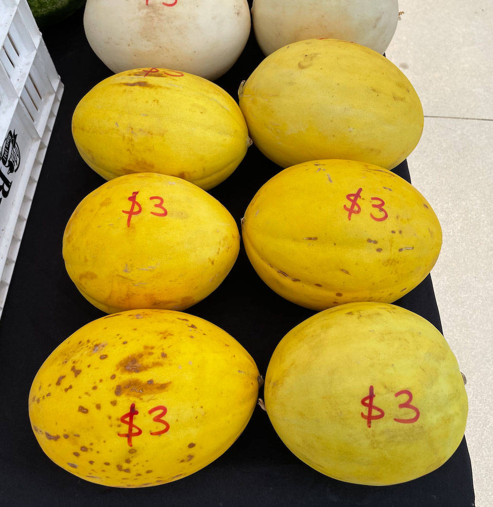 Fruit 桌布 壁紙 — 鮮黃色蜜瓜帶有紅色 $3 價格標籤，整齊排列在黑色表面上，營造市場氛圍。