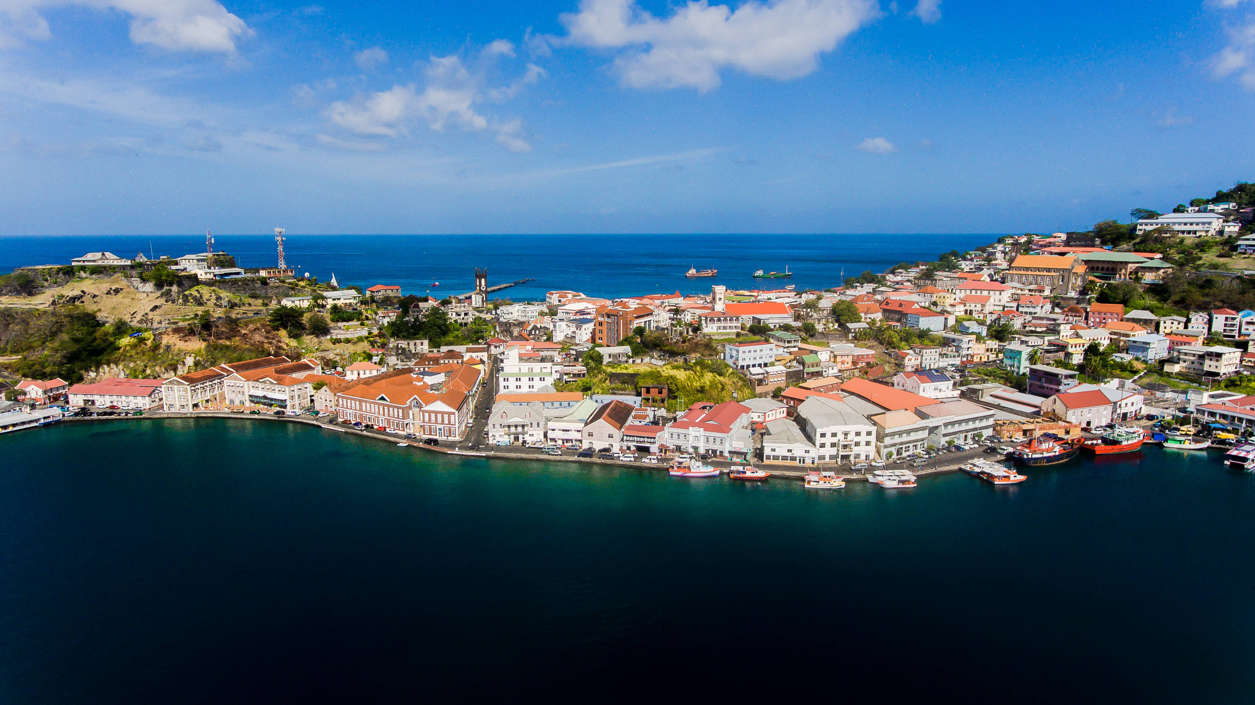 Grenada 桌布 壁紙 — 鳥瞰一個充滿活力的沿海小鎮，紅頂建築緊貼著深藍色的港灣，上方是明亮的藍天。